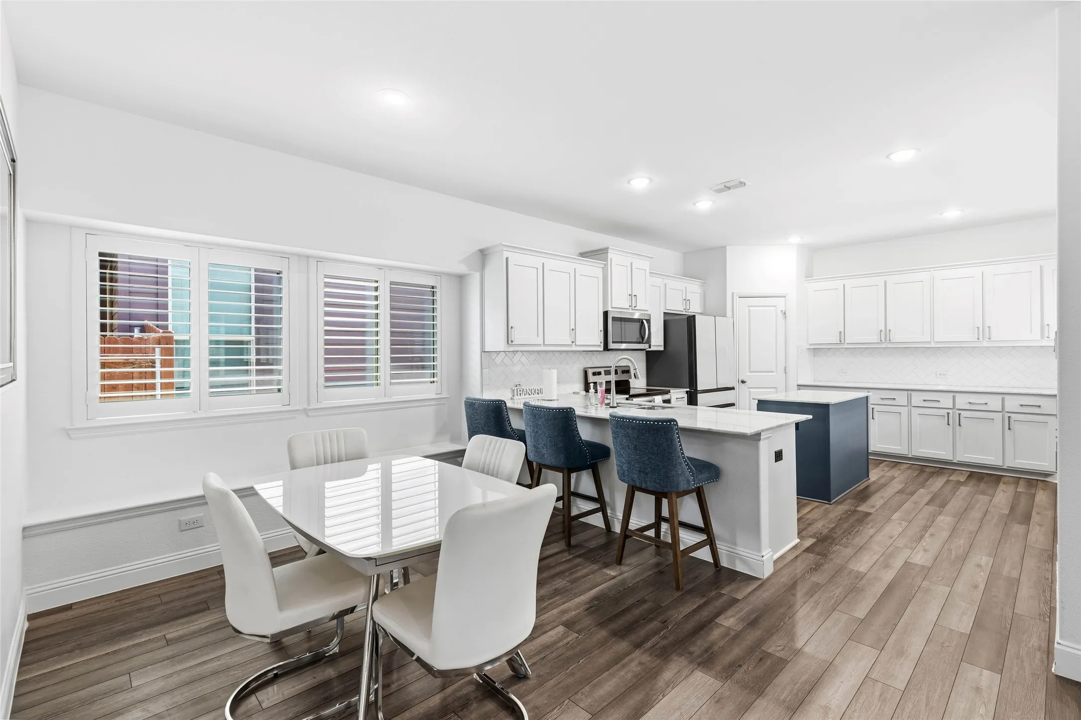 Open-concept kitchen and dining area featuring wood-finish flooring, white cabinetry, a kitchen island with seating, a secondary island, and recessed lighting