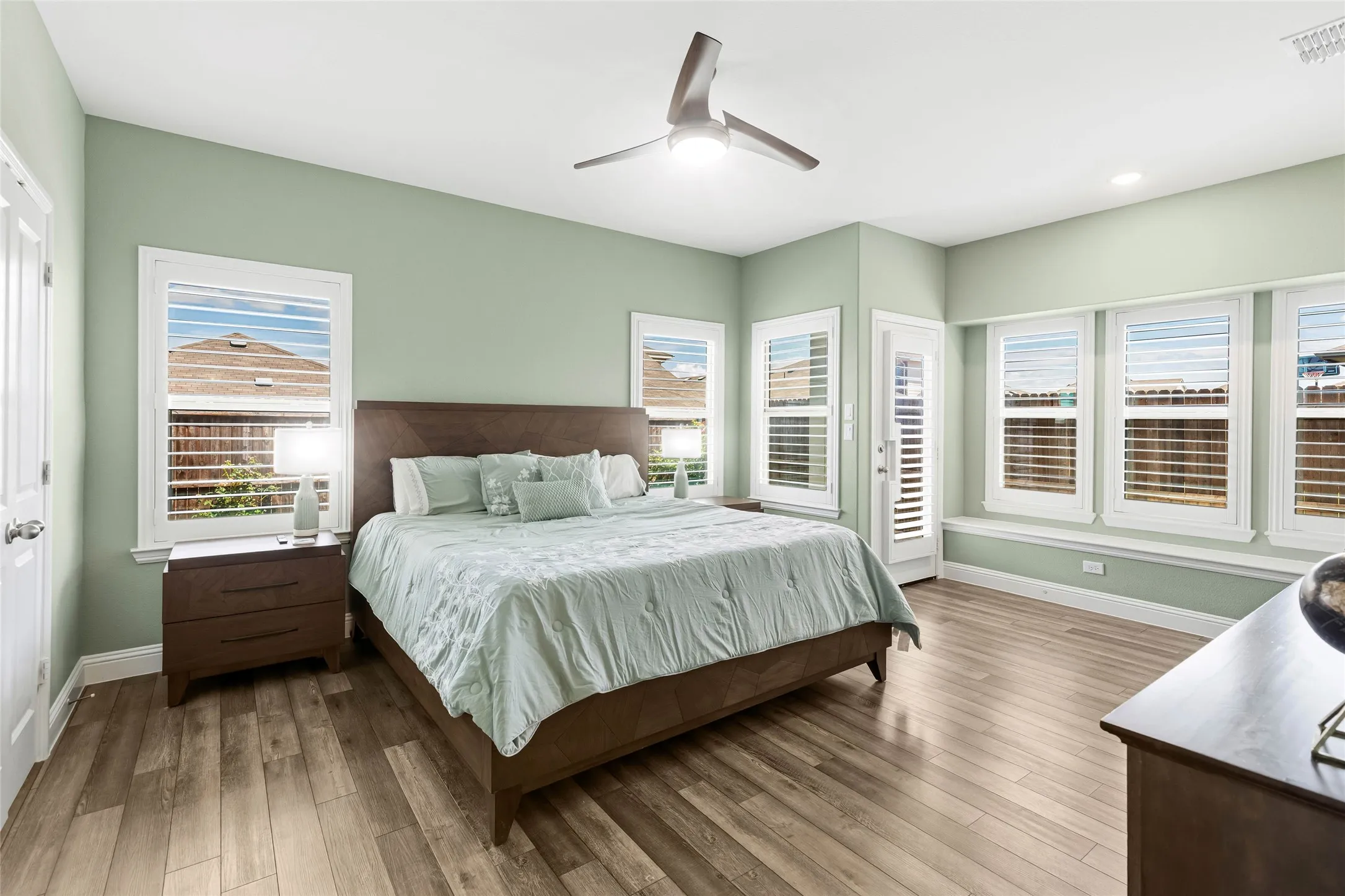 Spacious interior featuring wood-finish flooring, a contemporary ceiling fan, recessed lighting, multiple windows with white plantation shutters, and a white paneled door