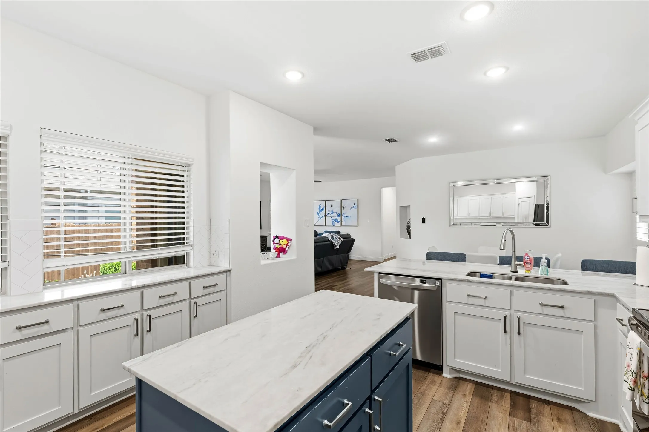 Bright kitchen featuring white cabinetry, light countertops, a central island with dark blue cabinetry, stainless steel appliances, and wood-finish flooring