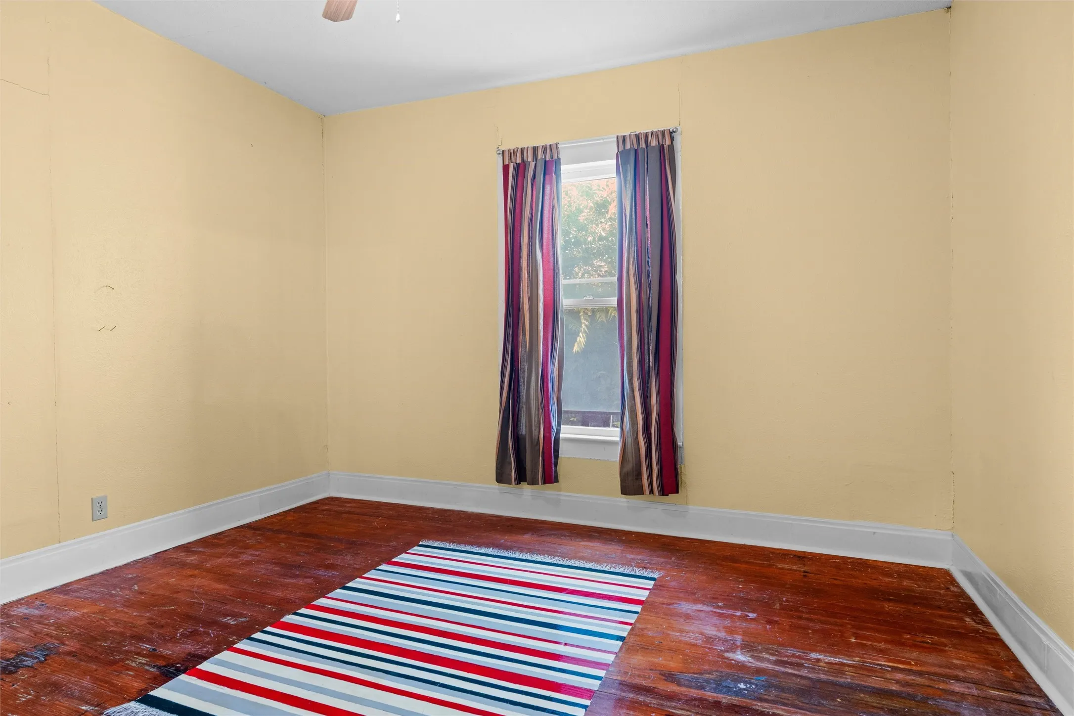 Room featuring wood-finish flooring, a single window, and a ceiling fan