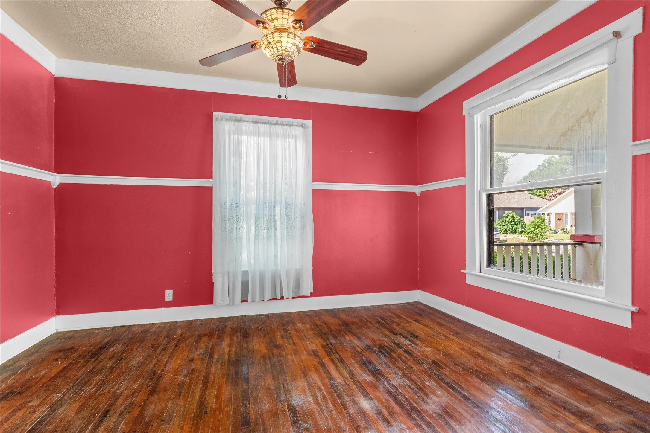 Hardwood flooring with a rich wood-finish, accented by white trim and a decorative ceiling fan with an illuminated Tiffany-style shade