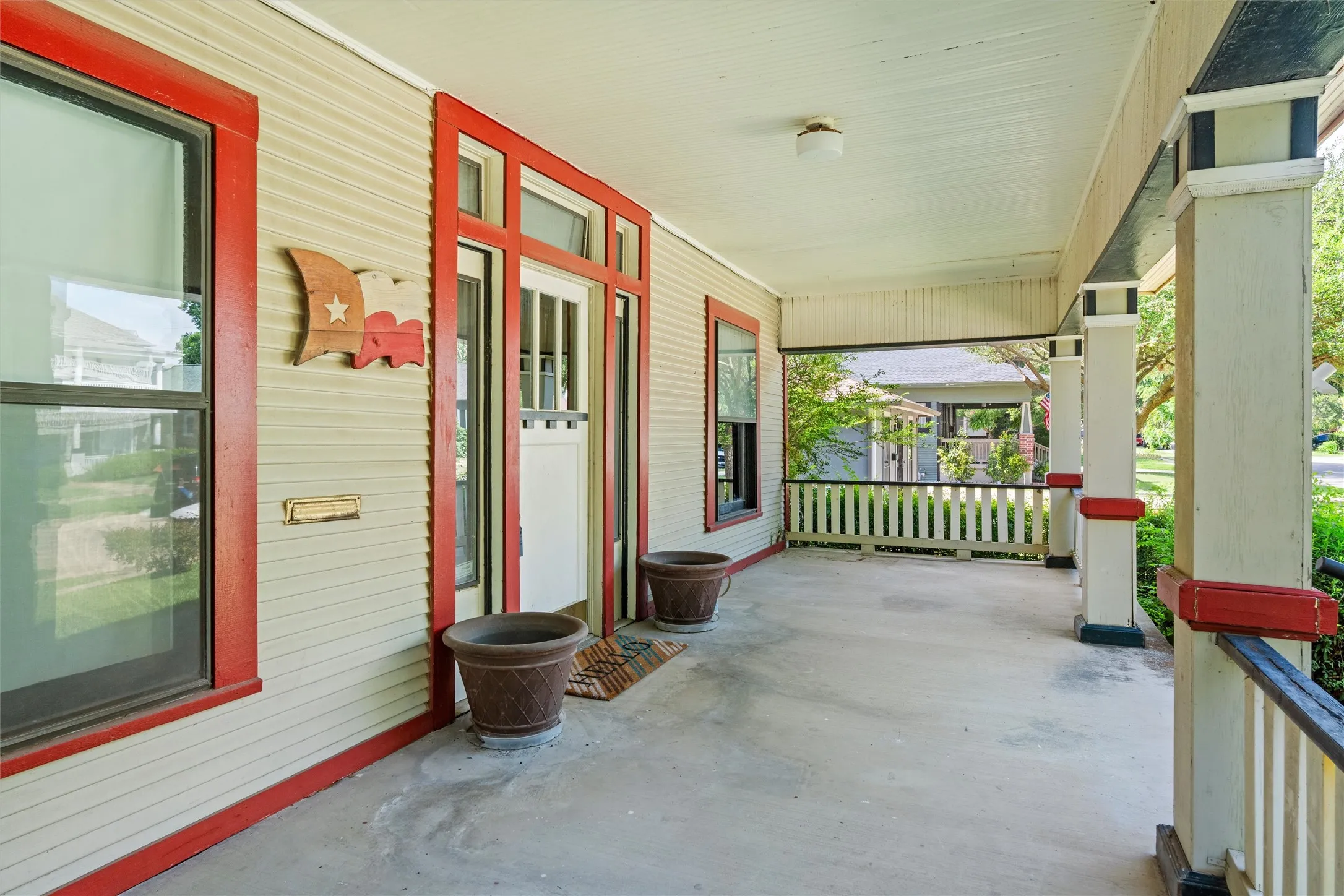 Expansive covered front porch featuring a concrete surface, painted railing, and substantial support columns