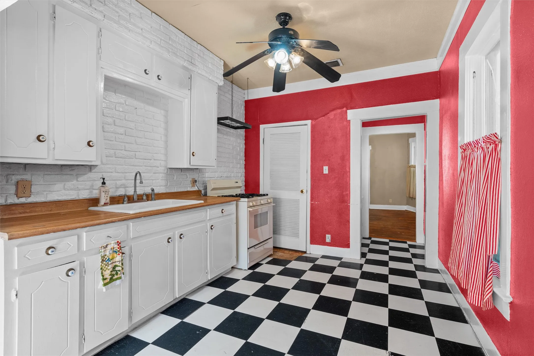 Kitchen featuring black and white checkerboard flooring, white cabinetry, wood-finish countertops, and a white brick-style backsplash
