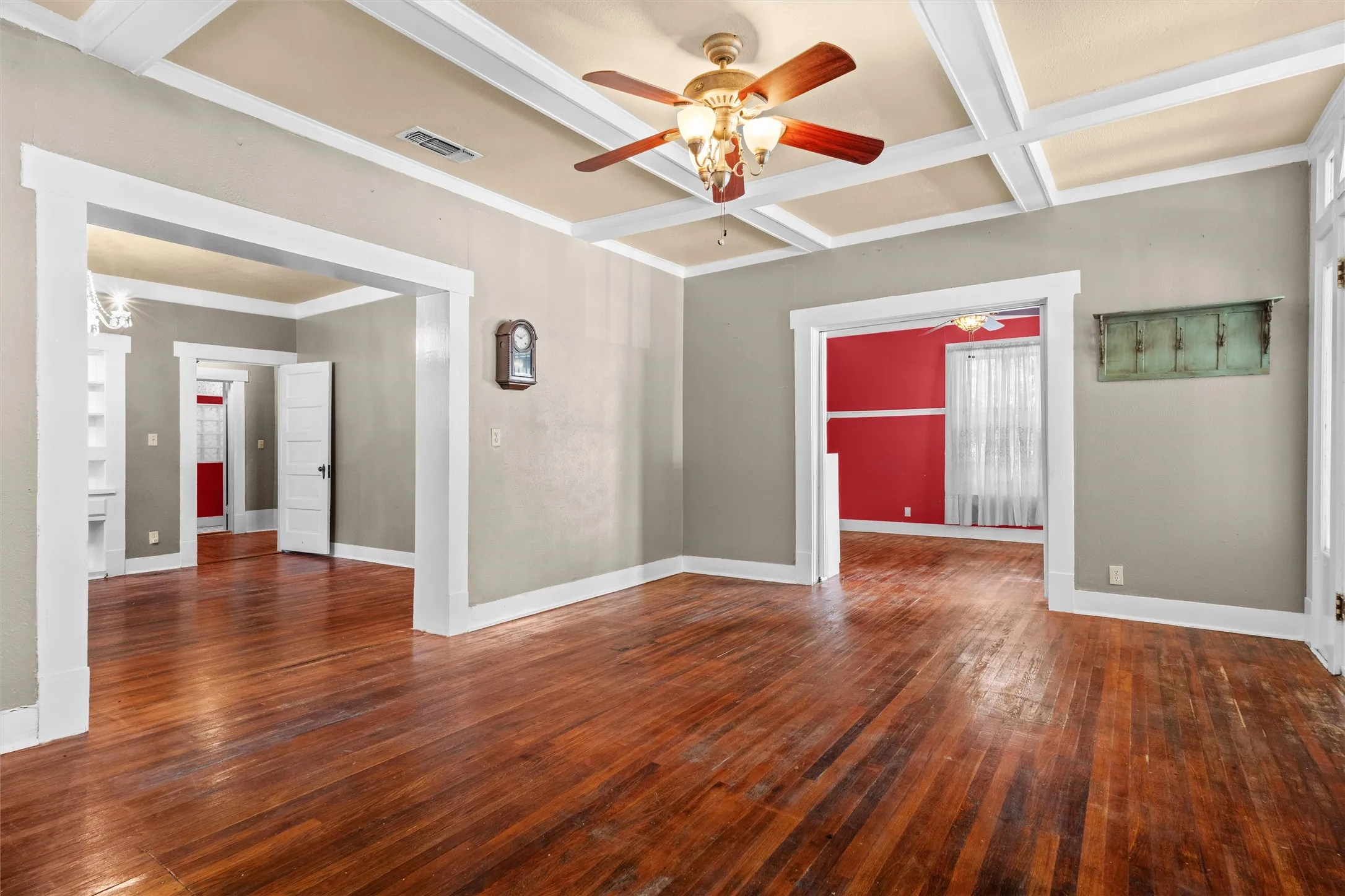 Spacious room featuring wood-finish flooring, a coffered ceiling with a ceiling fan, wide baseboards, and substantial door casings