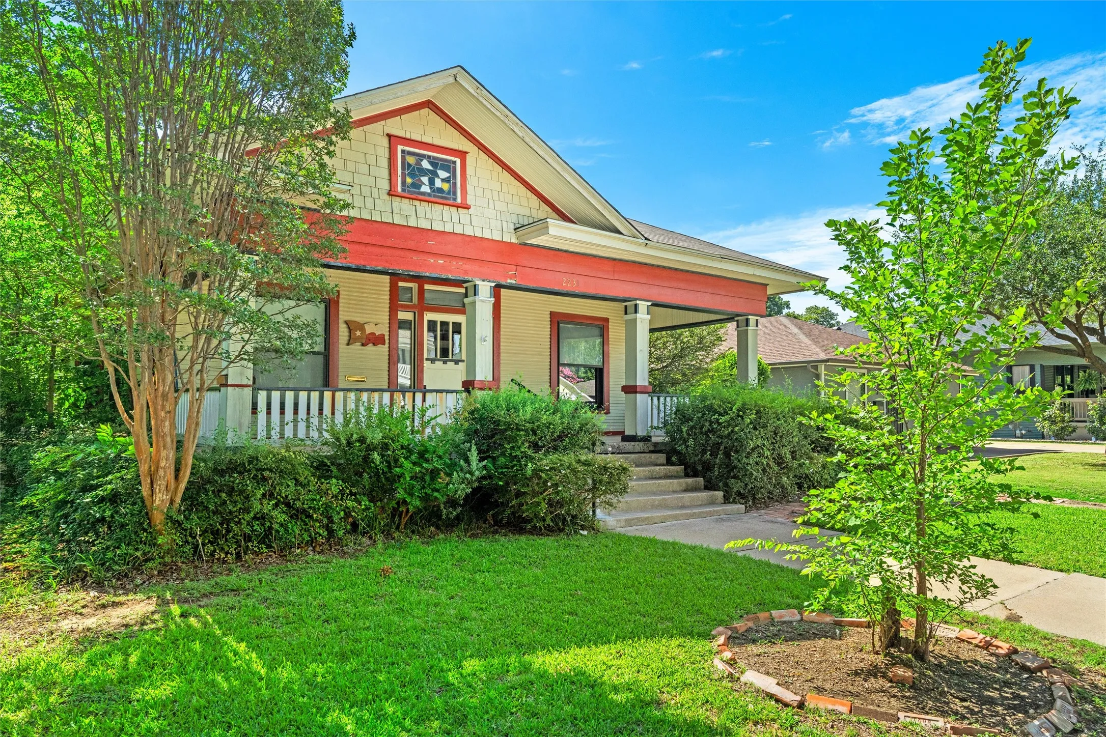 Craftsman-style home featuring a covered front porch with white railings, a prominent red trim, and a decorative attic window