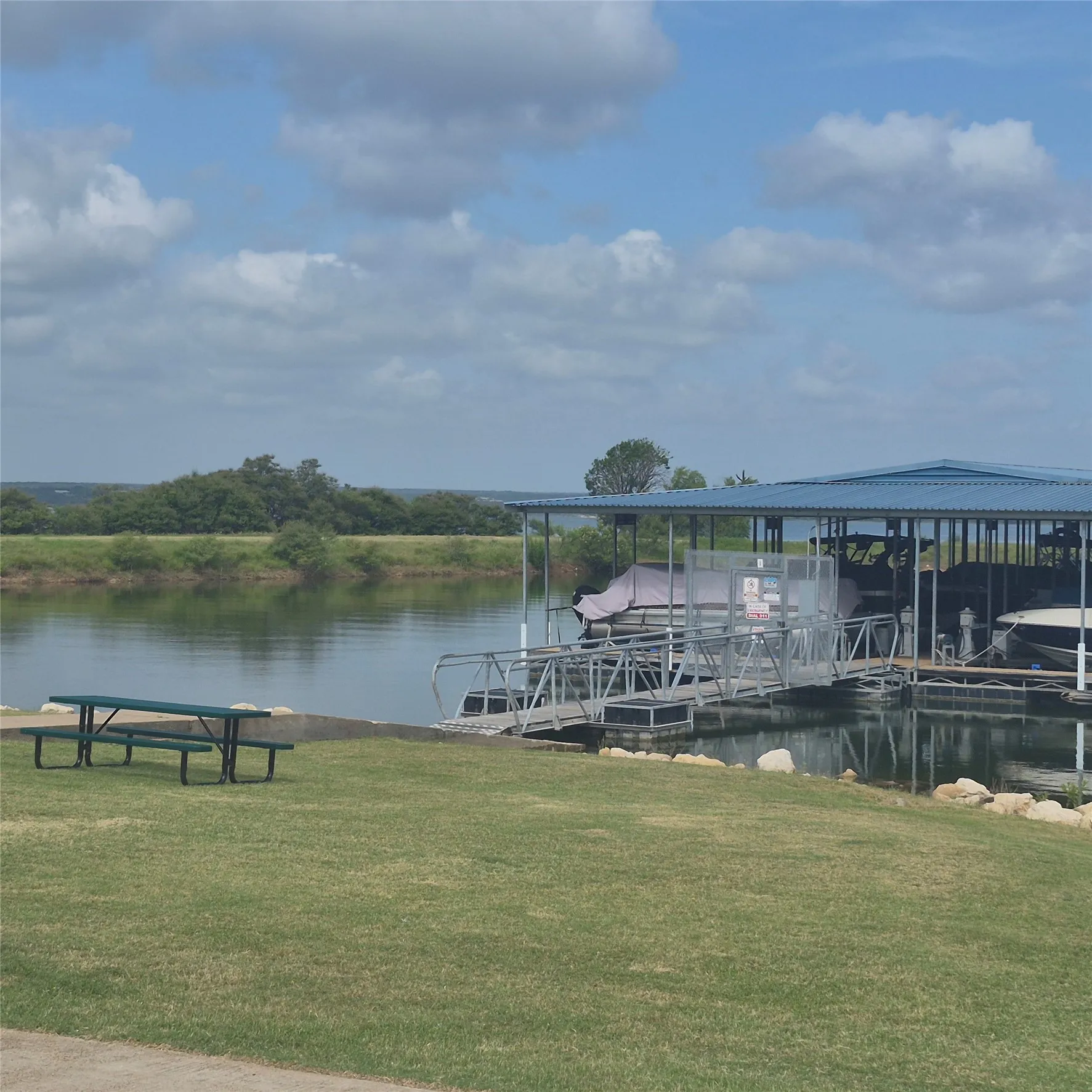 Waterfront property featuring a covered boat dock with multiple slips, a metal walkway, and a grassy area