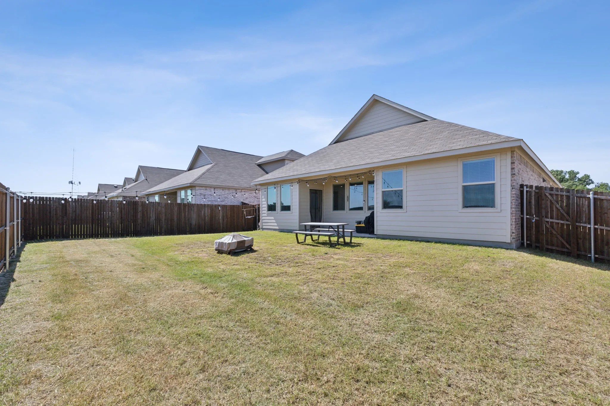 Expansive backyard featuring a full perimeter privacy fence, a concrete patio, and exterior string lighting along the rear of the residence