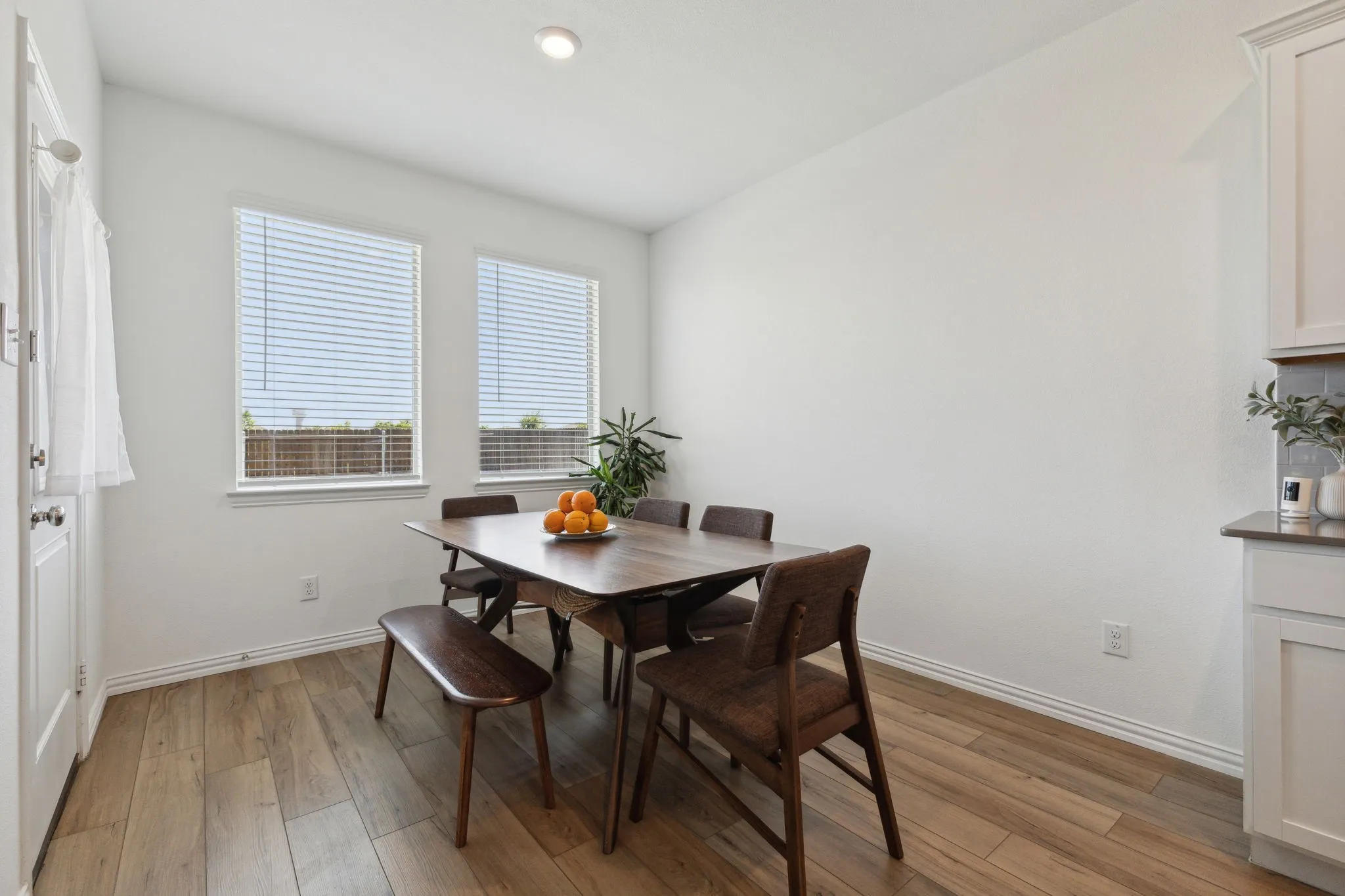 Bright dining area featuring wood-finish flooring, two large windows with blinds, a recessed ceiling light, and white baseboards