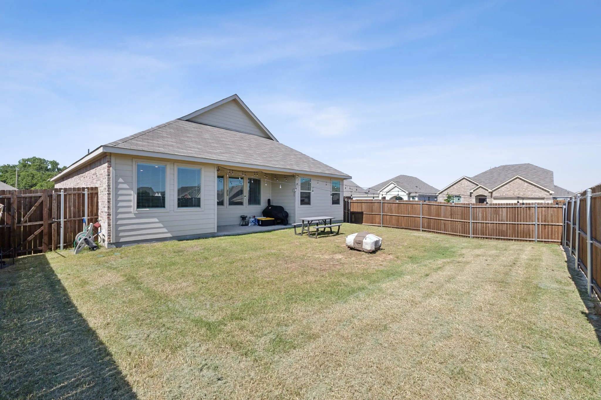 Expansive backyard featuring a manicured lawn, full privacy fencing, and a concrete patio