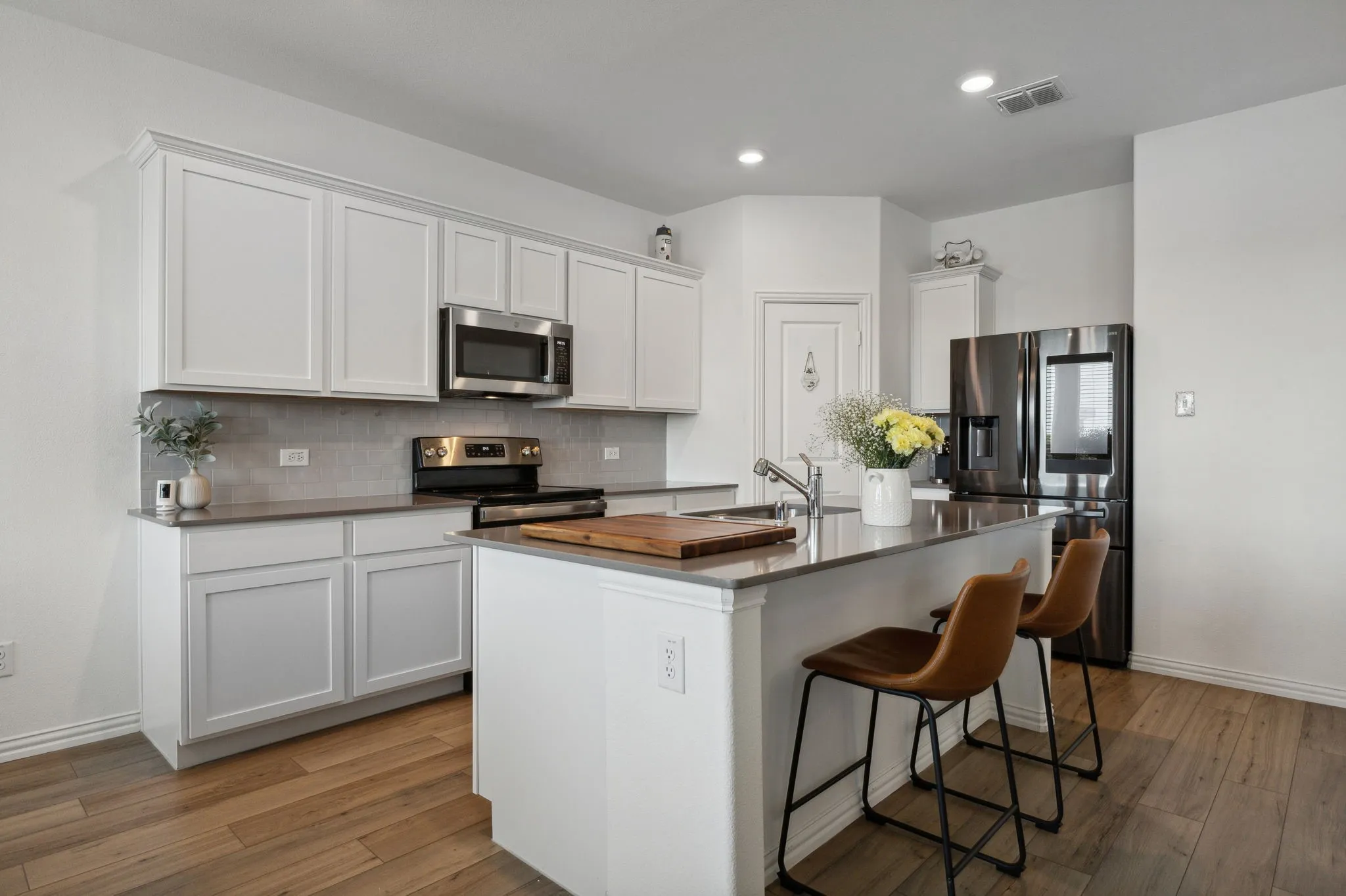 Kitchen featuring white shaker-style cabinetry, stainless steel appliances, a center island with an undermount sink, solid surface countertops, and wood-finish flooring
