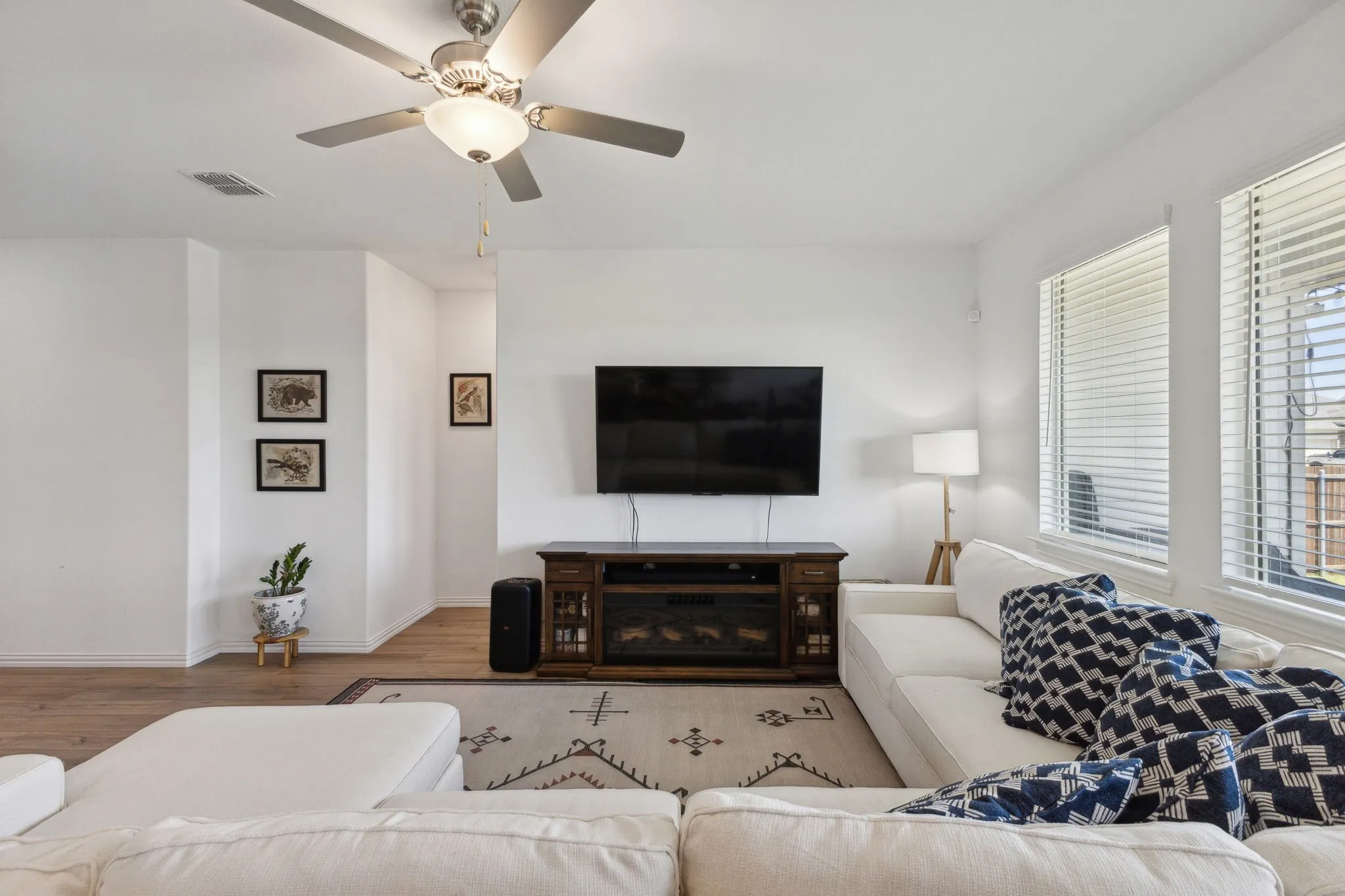 Bright living area featuring wood-finish flooring, a ceiling fan with integrated lighting, and multiple windows with blinds