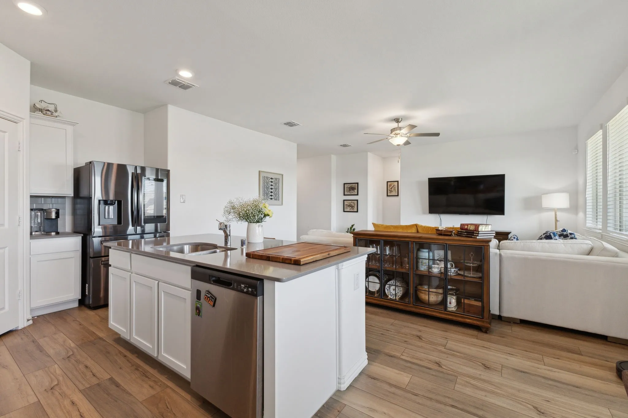 Open-concept living area featuring wood-finish flooring, a kitchen island with integrated sink and dishwasher, stainless steel appliances, and abundant natural light from multiple windows
