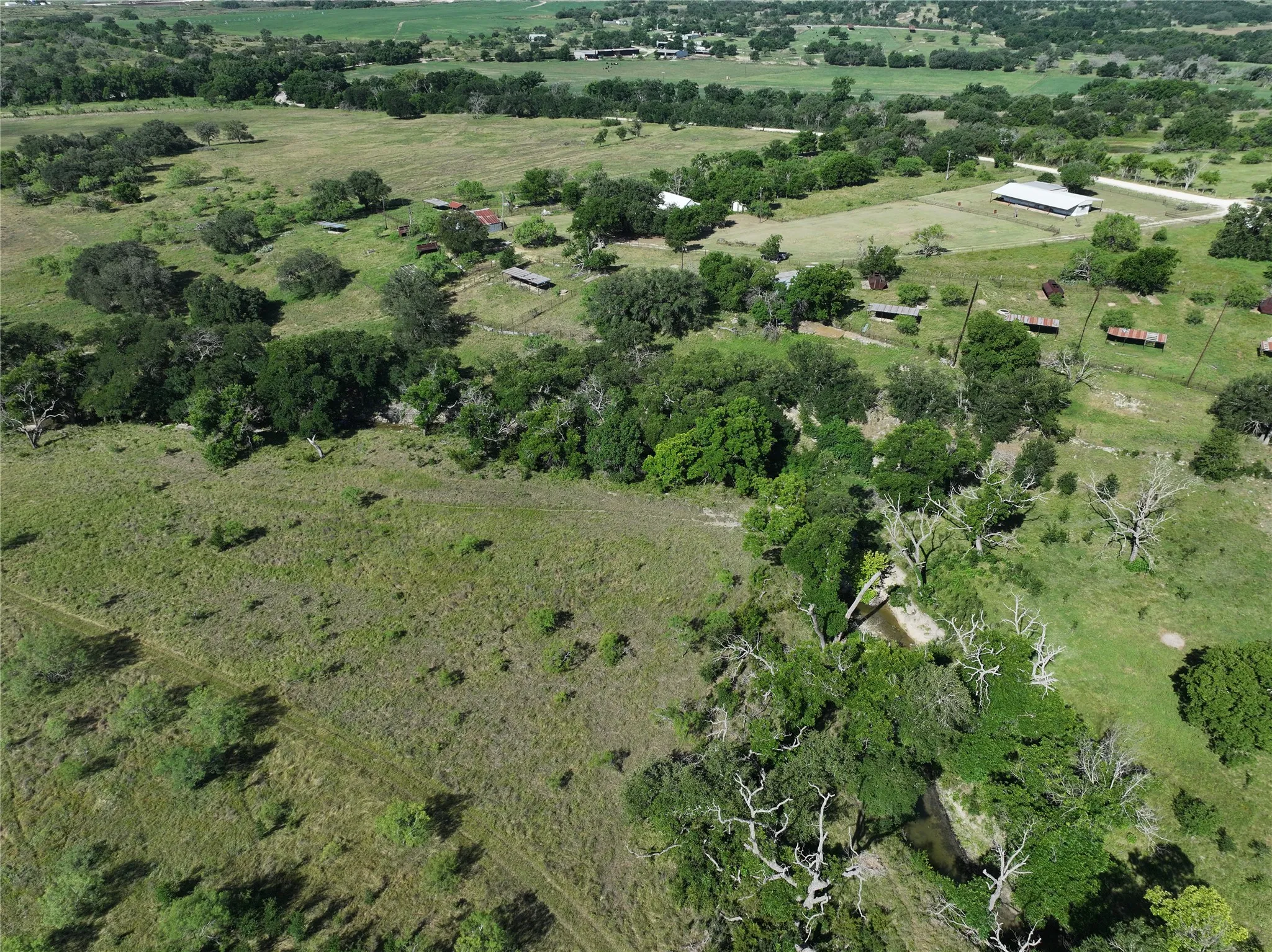 Expansive open fields with scattered trees and a natural creek winding through the landscape