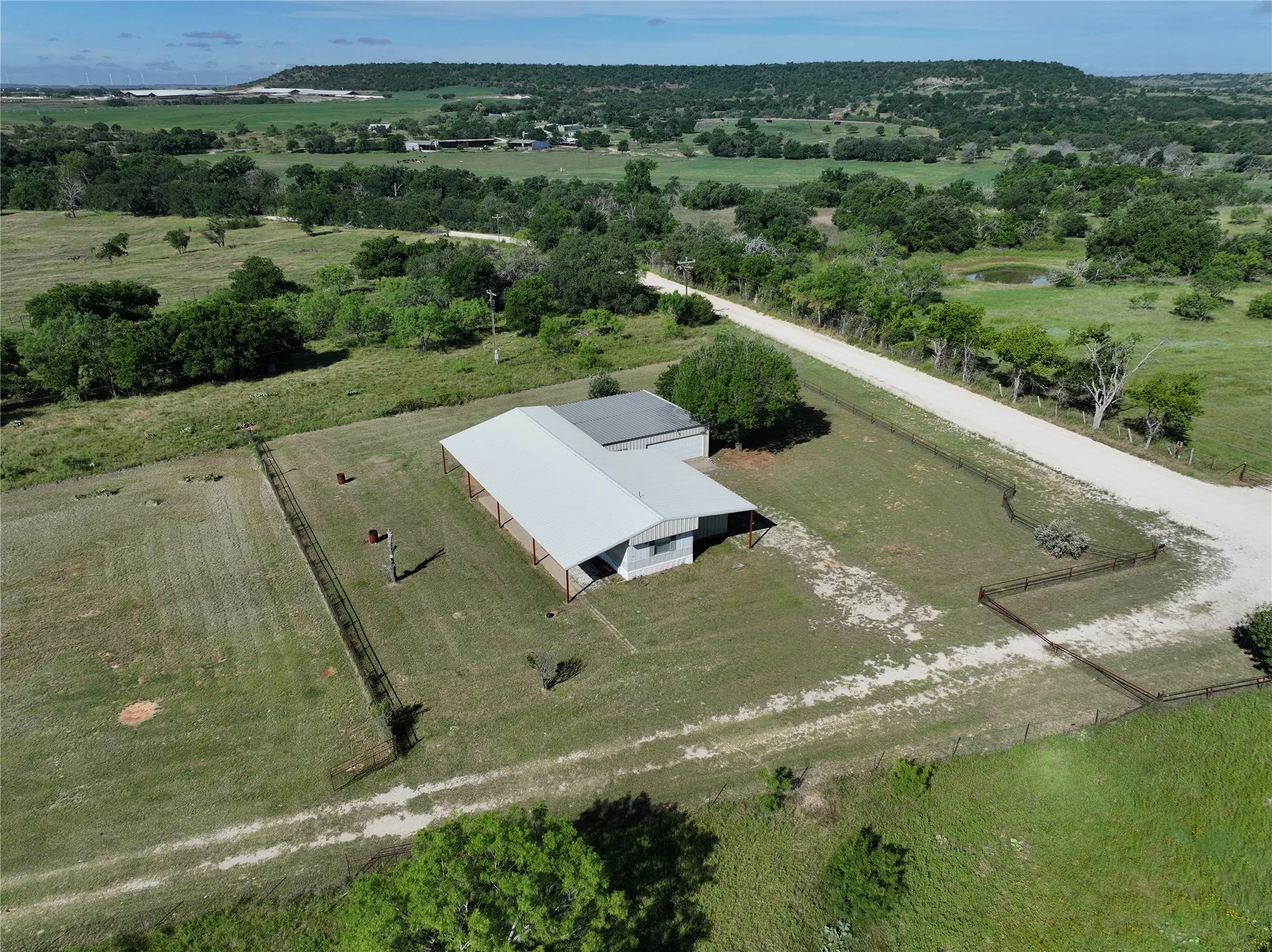 Expansive agricultural property featuring a single wide, with an attached covered structure, a winding dirt road, and multiple fenced areas