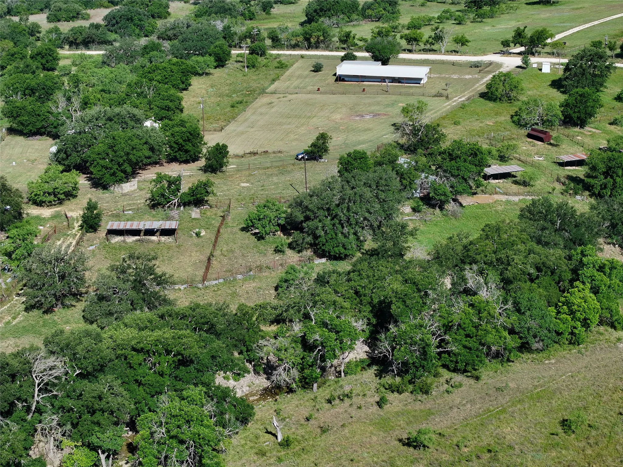 Expansive rural property featuring a main building with a light-colored roof, multiple outbuildings, and a fenced pasture area