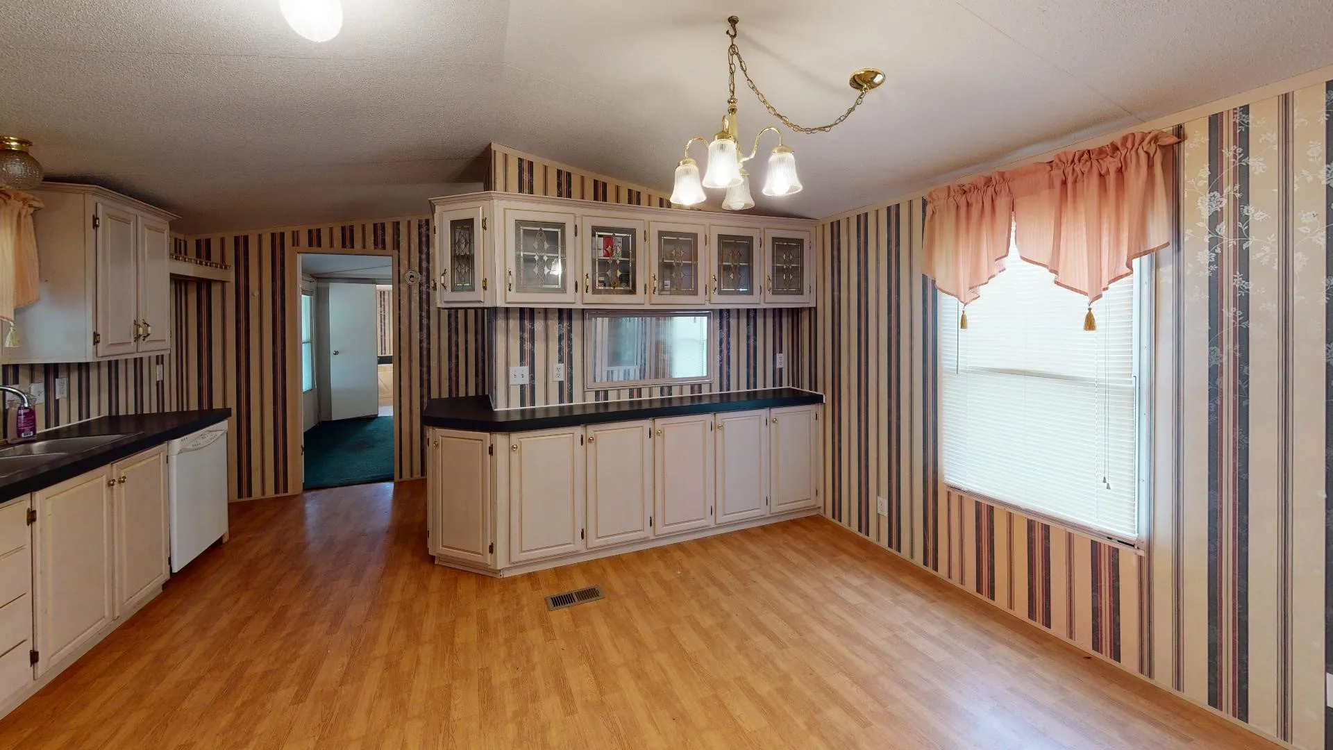 Single wides open-concept kitchen and dining area featuring wood-finish flooring, white cabinetry with dark countertops, built-in display cabinets, and an integrated kitchen sink