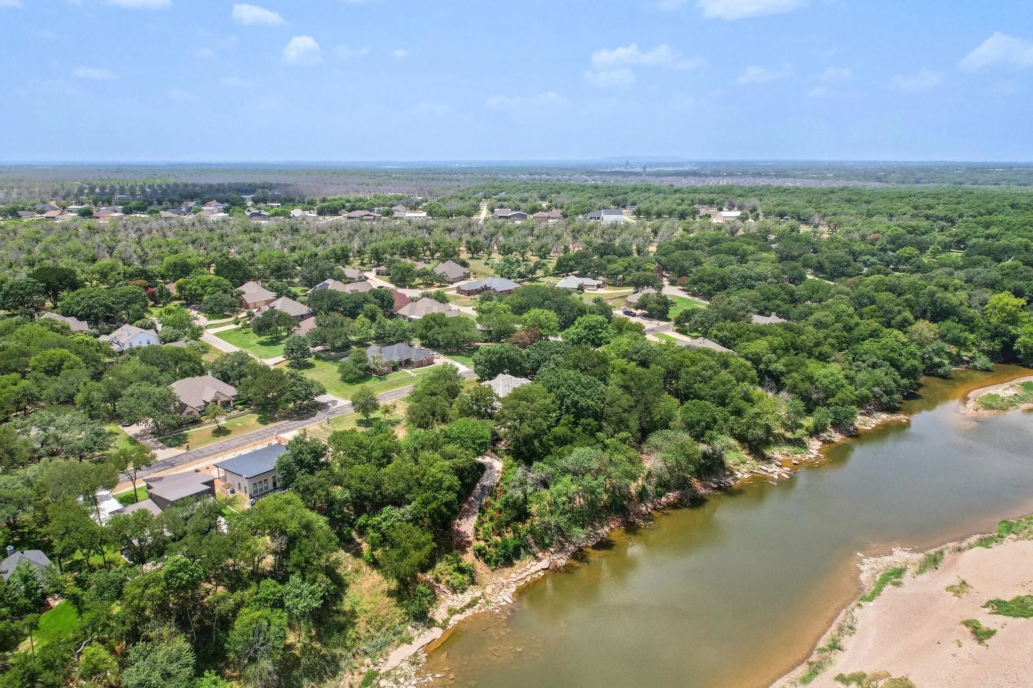 Expansive aerial showcasing a residential area bordered by a river and extensive tree coverage