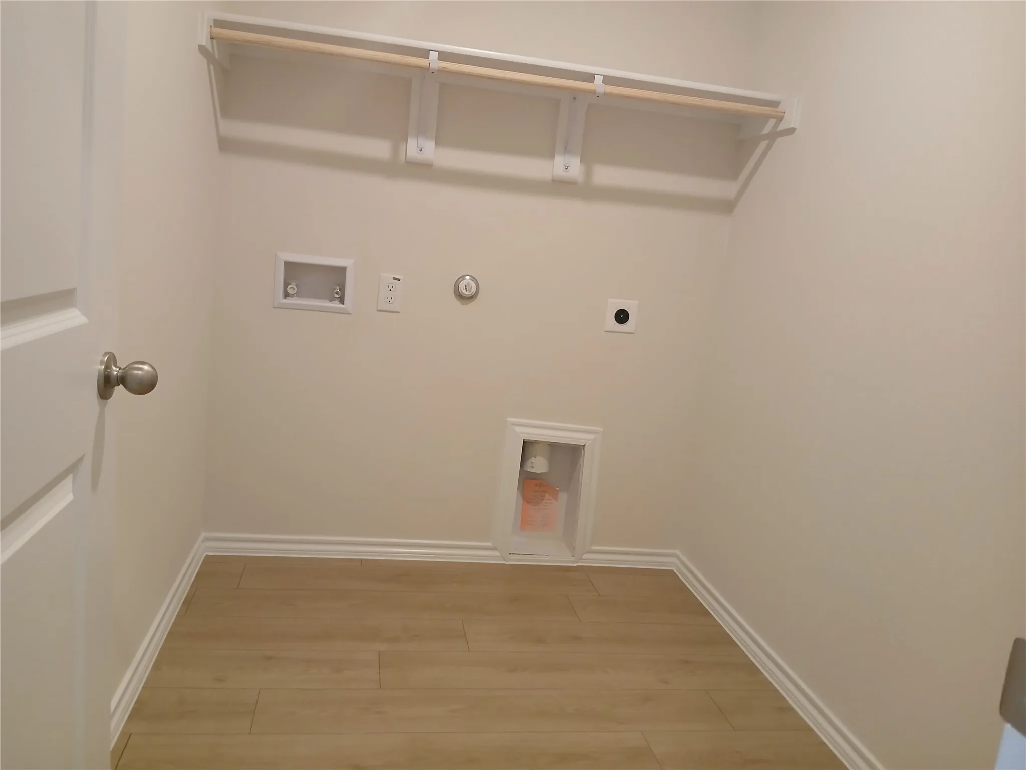 Dedicated laundry space featuring wood-finish flooring, white baseboards, and a built-in hanging rod