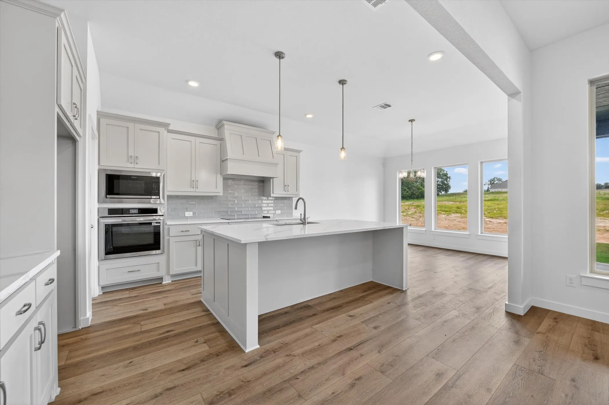 Contemporary kitchen featuring light gray cabinetry, built-in stainless steel appliances, a flush-mount cooktop, and a subway tile backsplash