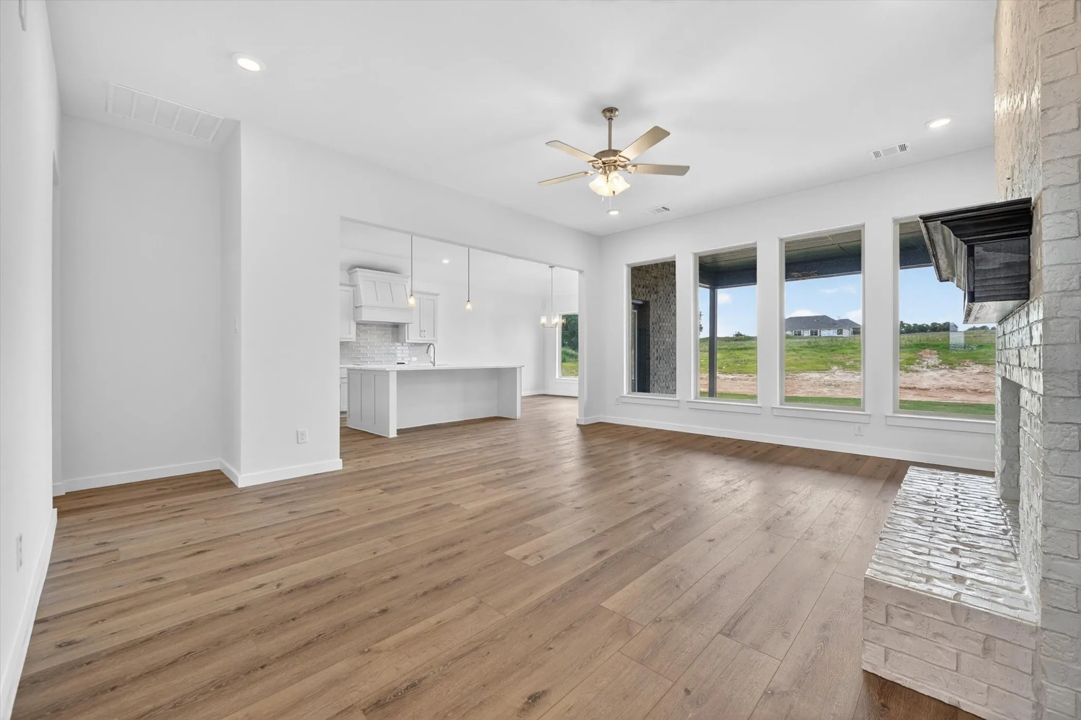 White brick-clad fireplace with wood mantle, wood-finish flooring, recessed lighting, and a ceiling fan