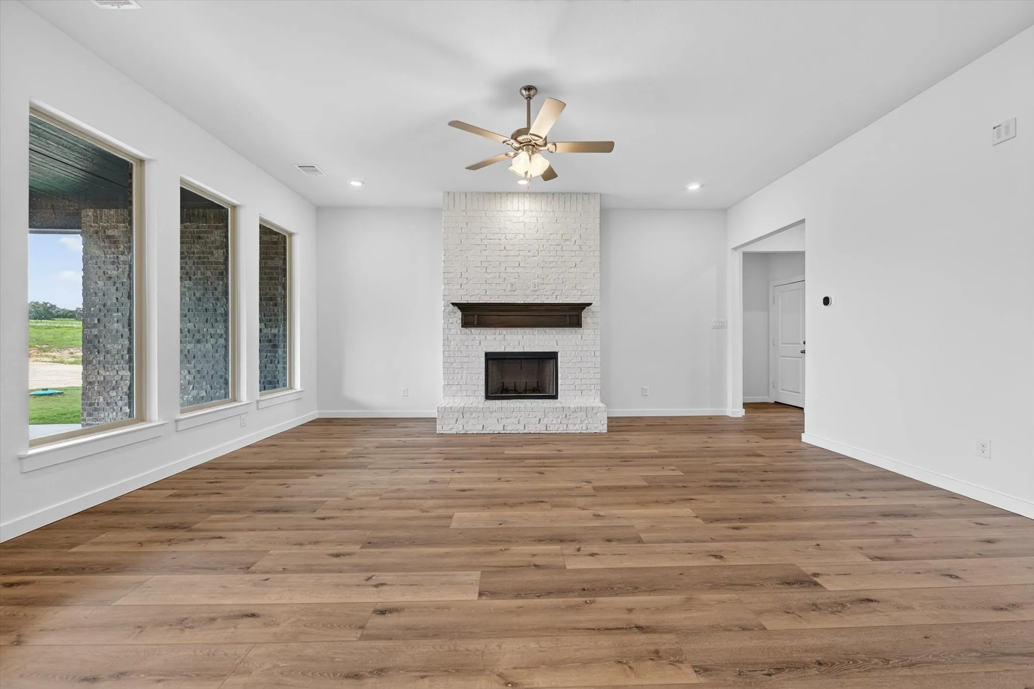 Open-concept living area with wood-finish flooring, a white brick fireplace, and recessed lighting