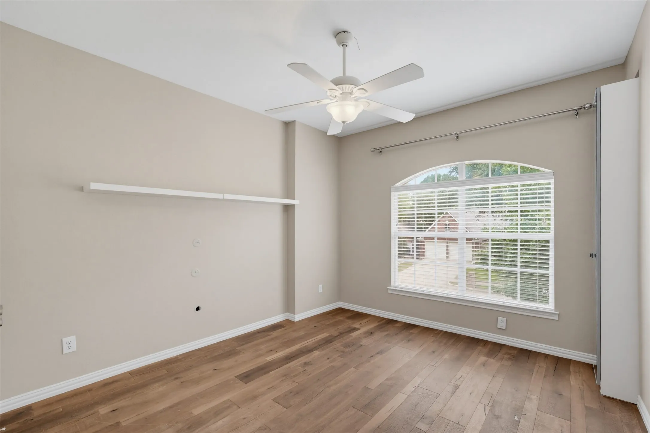 Room featuring wood-finish flooring, an arched window with blinds, a ceiling fan with integrated lighting, and a built-in wall shelf