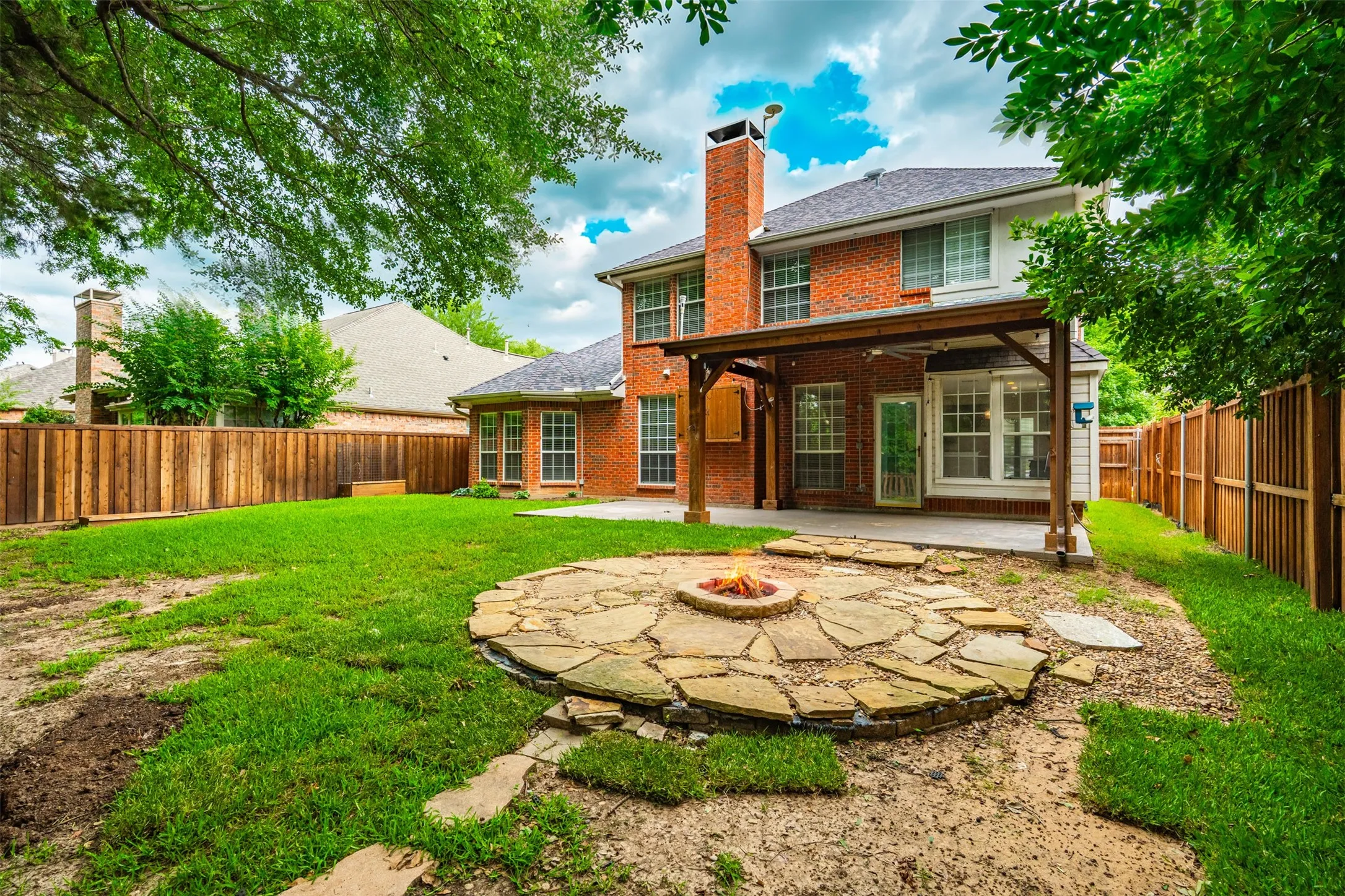 Expansive rear yard featuring a stone fire pit, covered patio, and privacy fencing