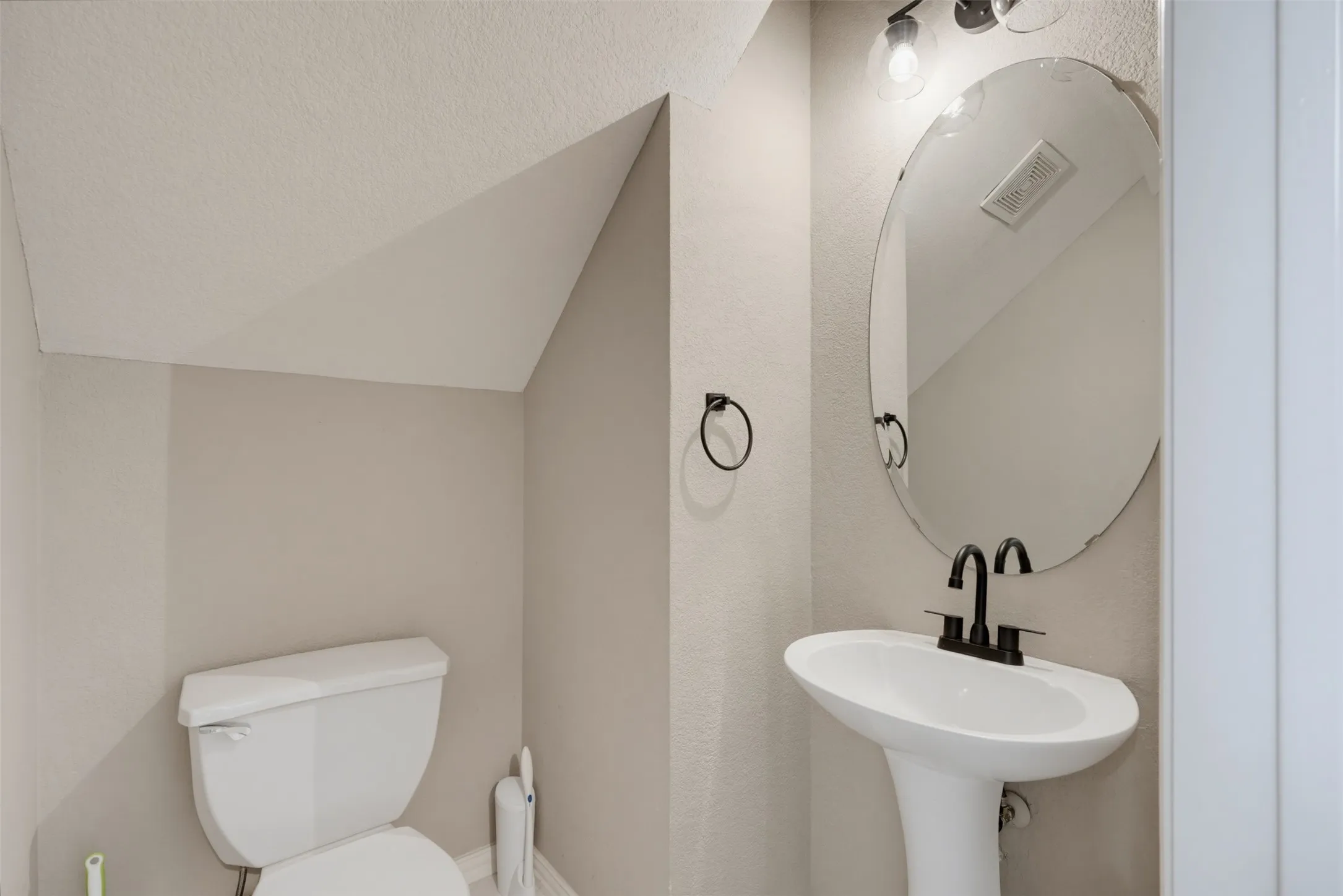Powder room featuring a pedestal sink with a matte black faucet, an oval frameless mirror, and a contemporary wall-mounted light fixture