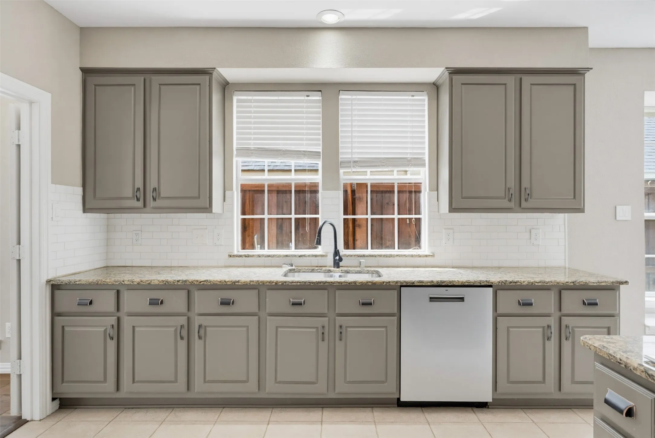 Kitchen featuring gray shaker-style cabinetry, light-toned granite countertops, and a white subway tile backsplash
