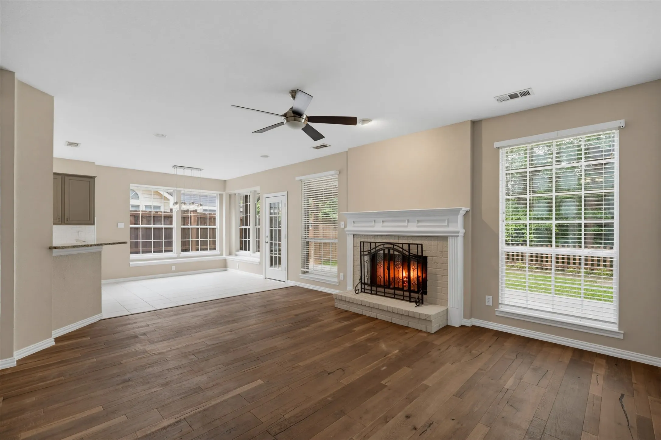 Living area featuring wood-finish flooring, a white brick fireplace with a detailed mantel, and a ceiling fan