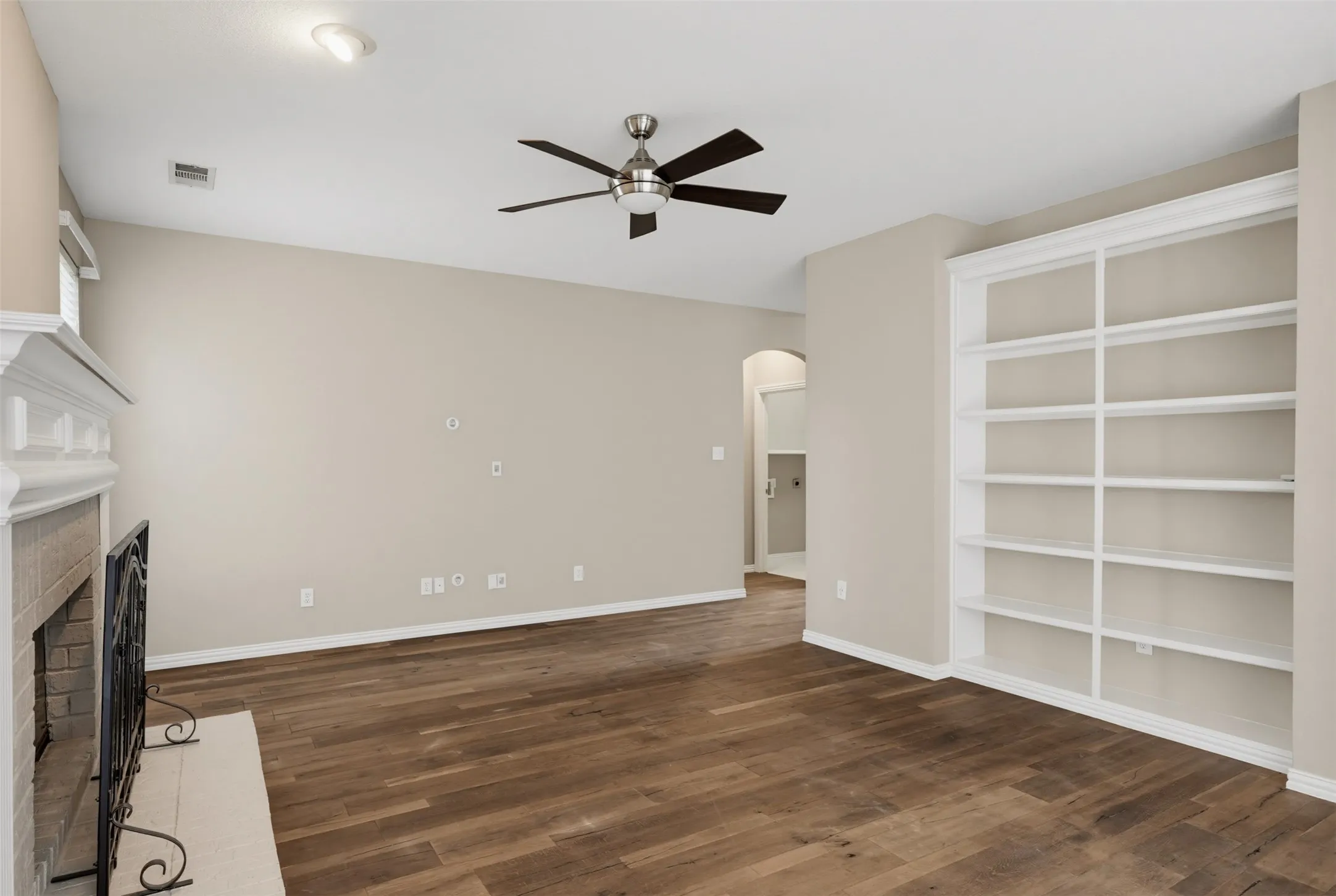 Spacious room featuring wood-finish flooring, a built-in bookshelf, and a fireplace with a detailed mantel