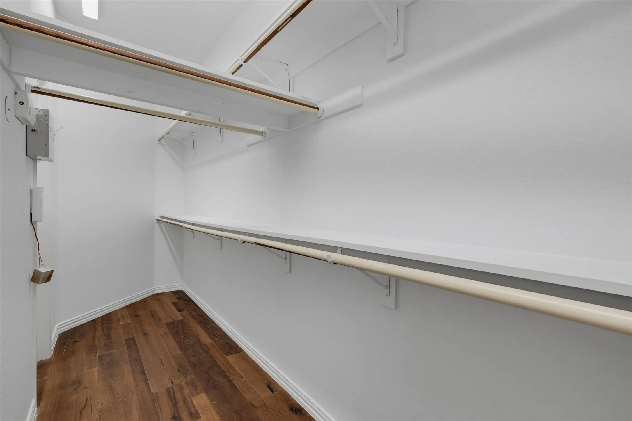 Walk-in closet featuring wood-finish flooring, white baseboards, white walls, multiple built-in shelving units, and integrated hanging rods