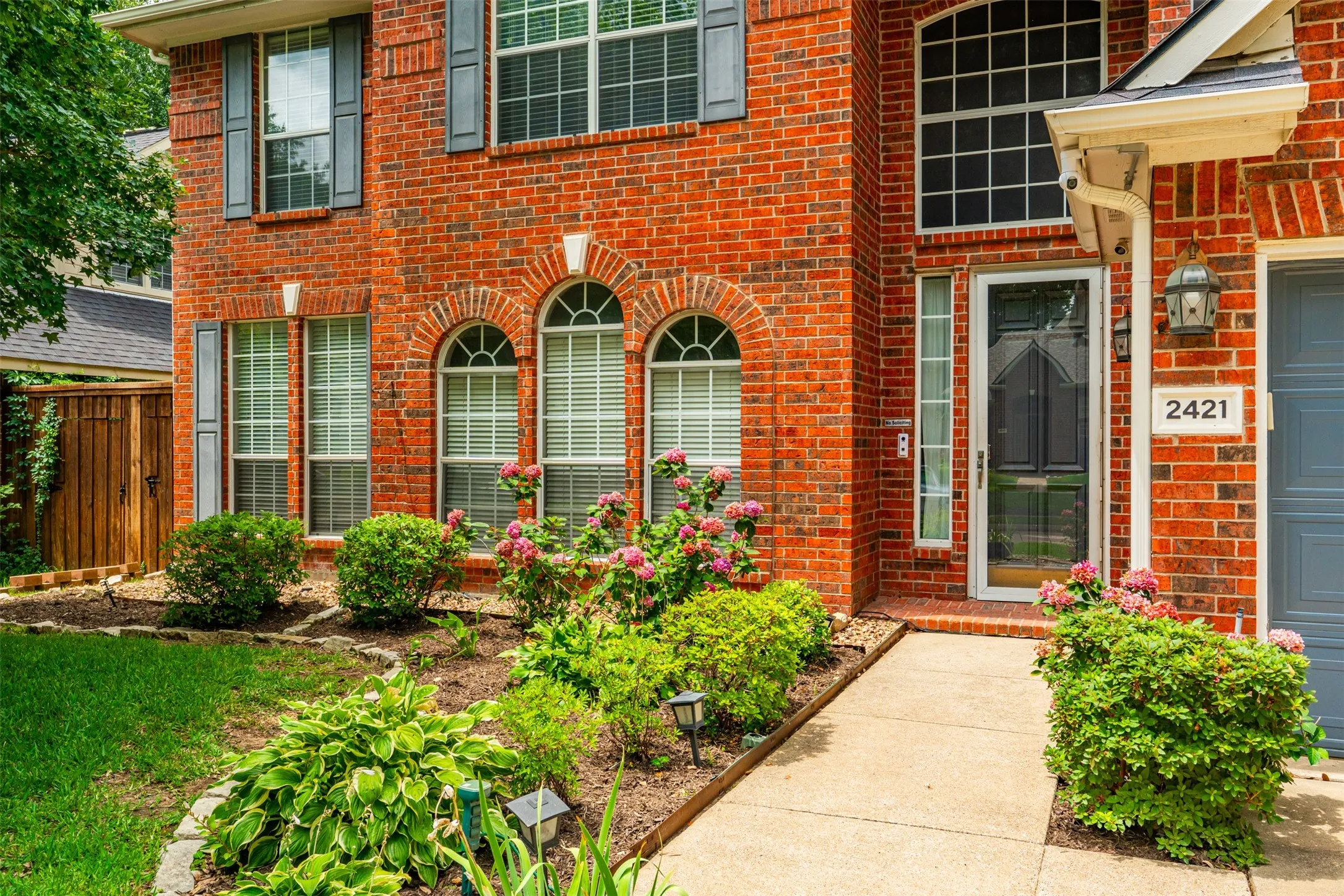 Red brick facade featuring arched windows, dark louvered shutters, and a prominent entry
