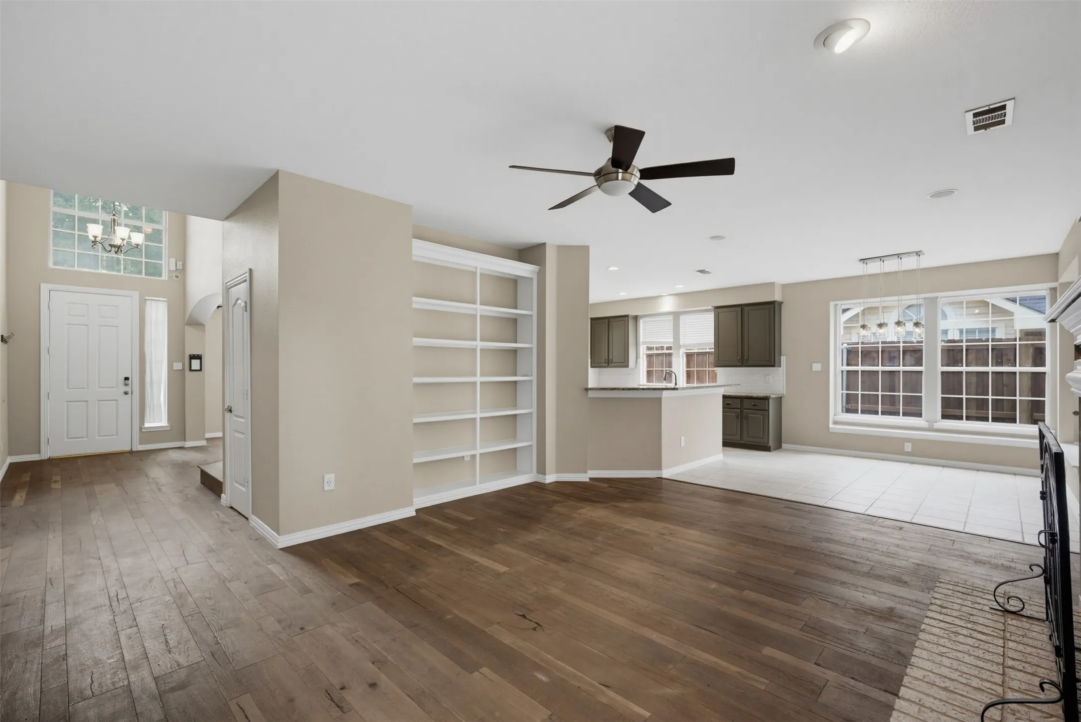 Expansive open-concept living area featuring wood-finish flooring, built-in shelving, and a ceiling fan