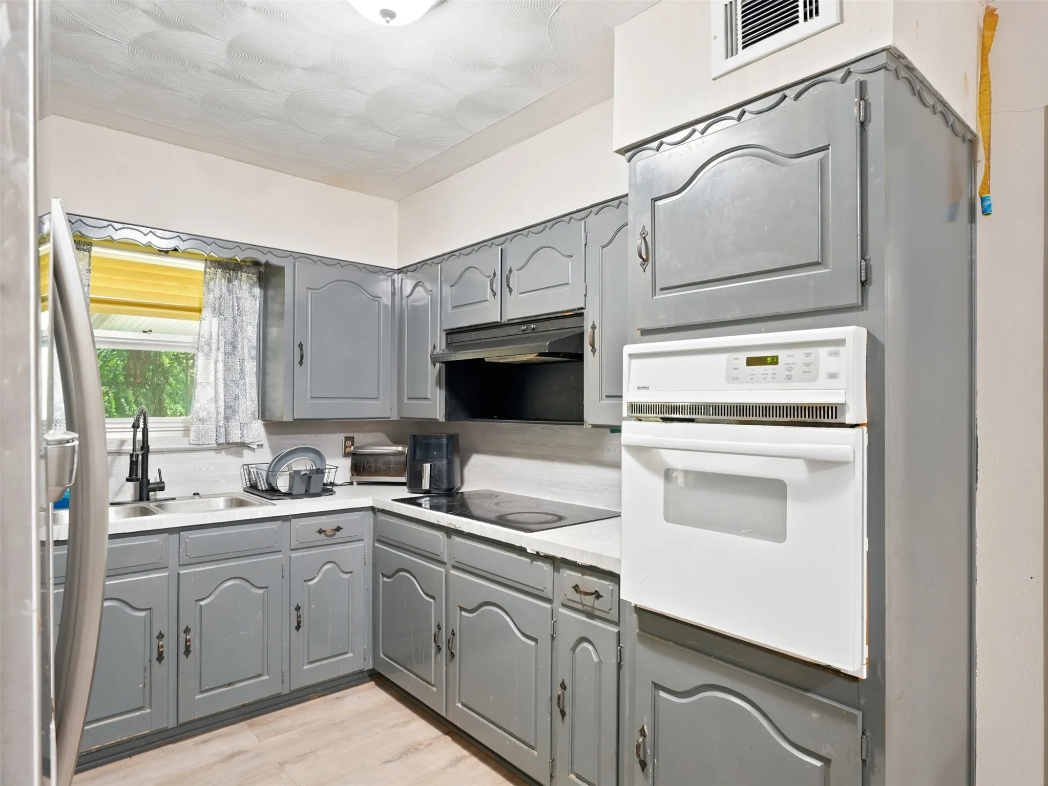 Kitchen featuring light gray cabinetry with decorative trim, a built-in wall oven, and a black cooktop