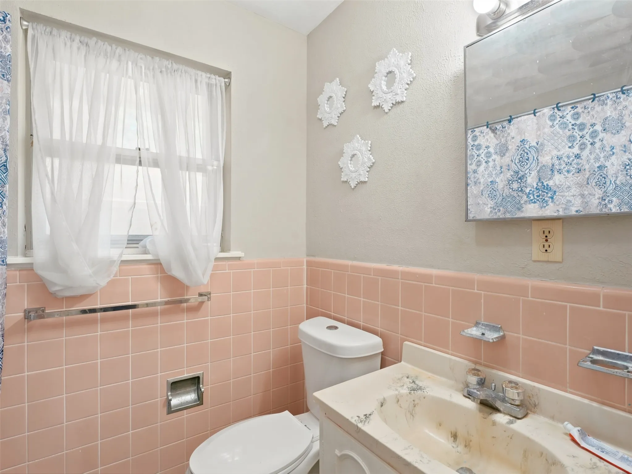 Bathroom featuring pink ceramic wall tile, window with sheer curtains, built-in vanity with sink, toilet, and mirrored medicine cabinet