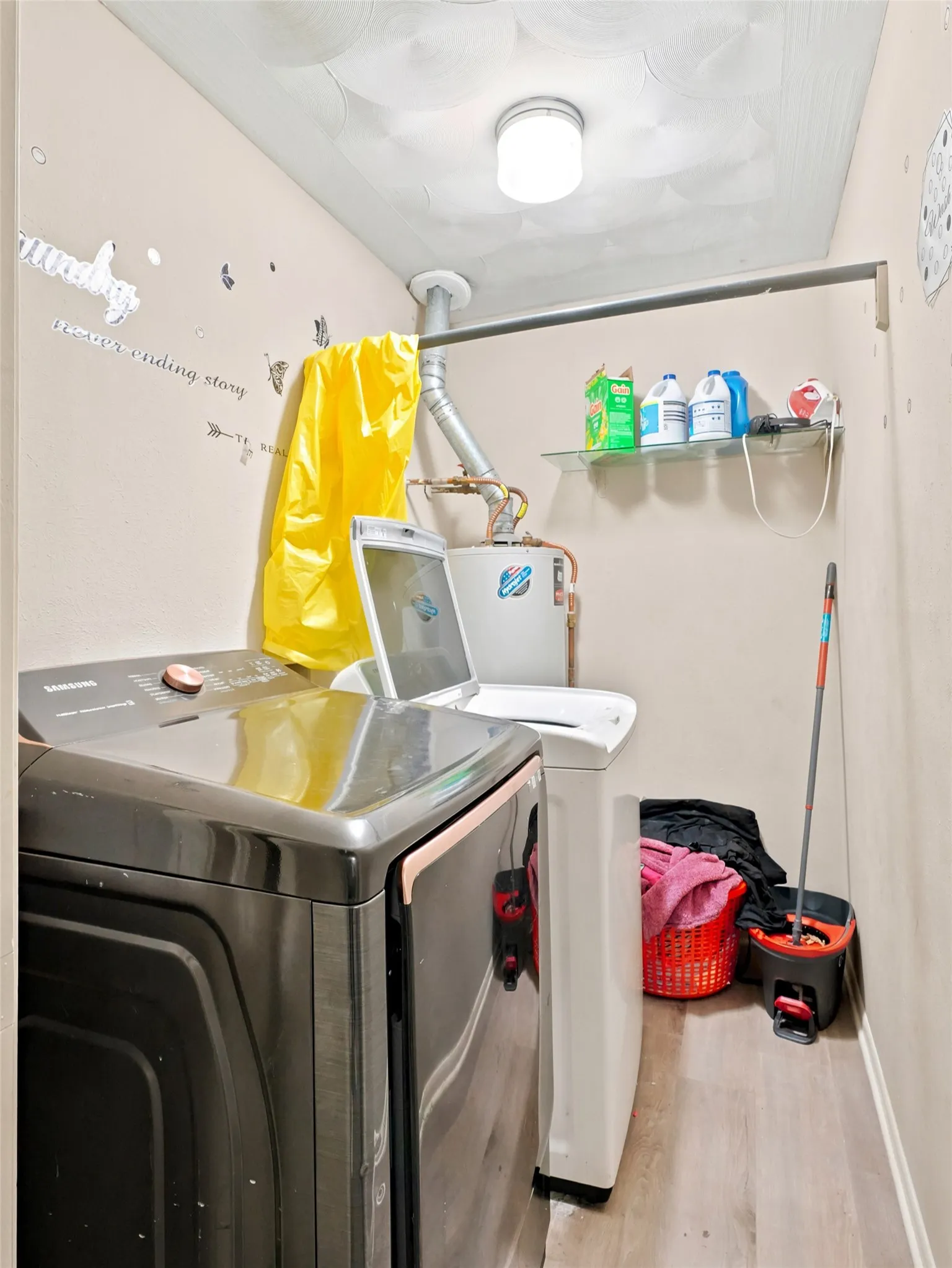 Dedicated laundry area featuring wood-finish flooring, a ceiling-mounted light fixture, and a wall-mounted shelving unit