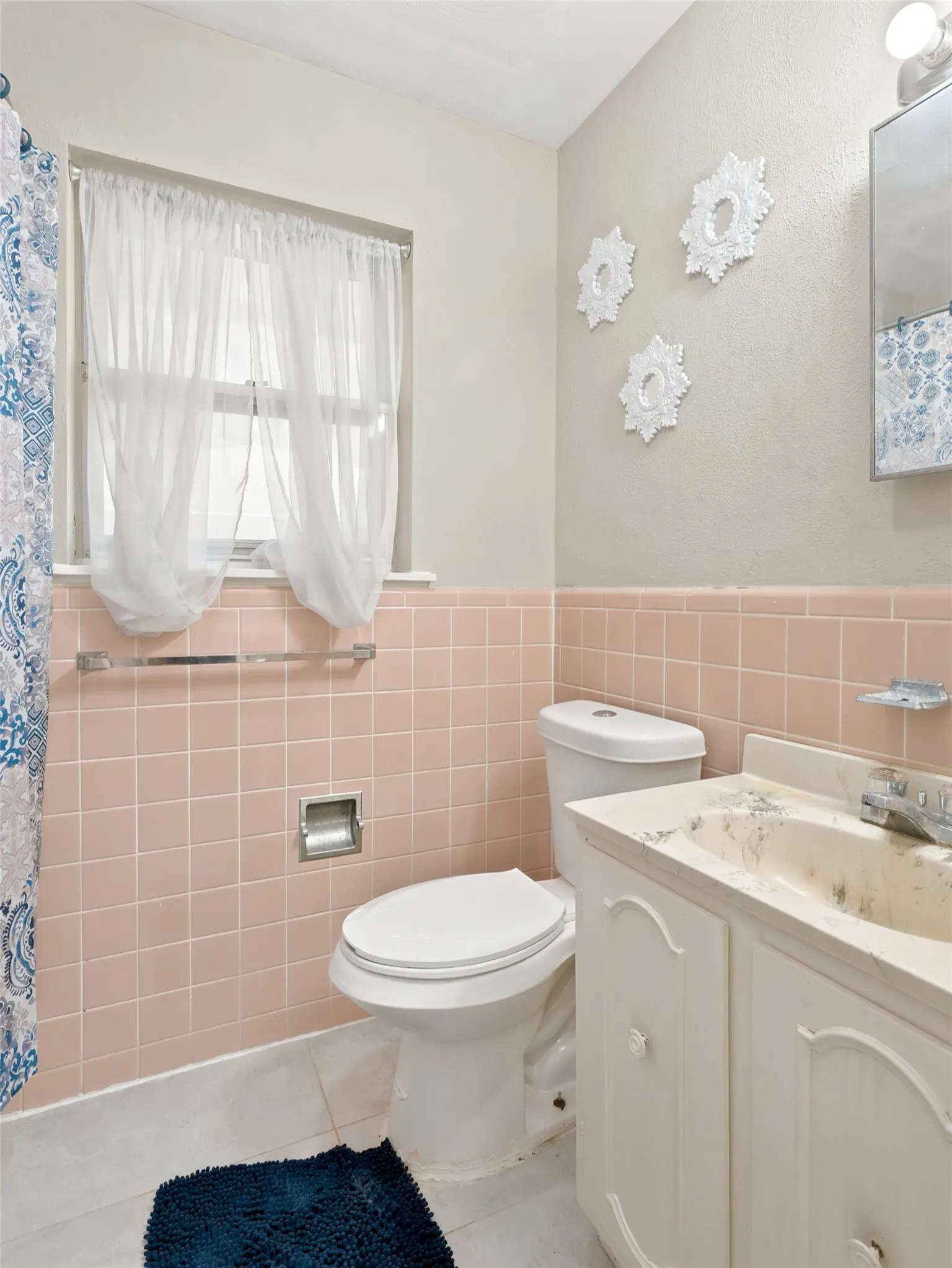 Bathroom featuring a window, pink tiled wainscoting, white floor tiles, a toilet, and a vanity with an integrated sink