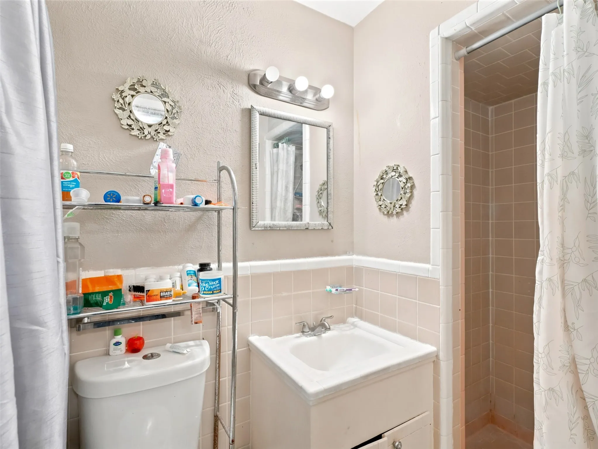 Bathroom featuring a vanity with an integrated sink, a wall-mounted mirror, and a shower enclosure with tiled walls