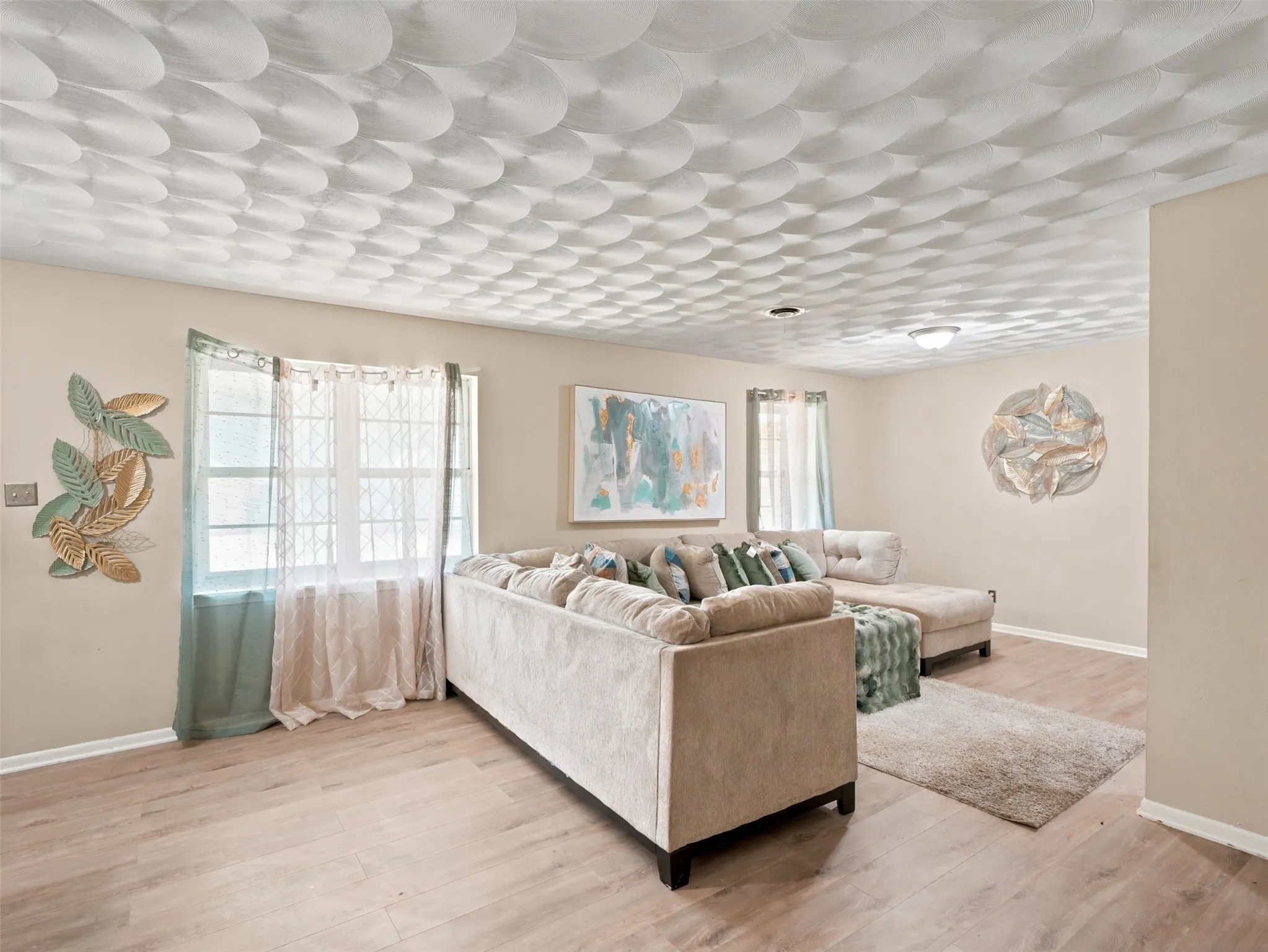 Living area showcasing a unique textured ceiling design, light wood-finish flooring, and neutral wall tones