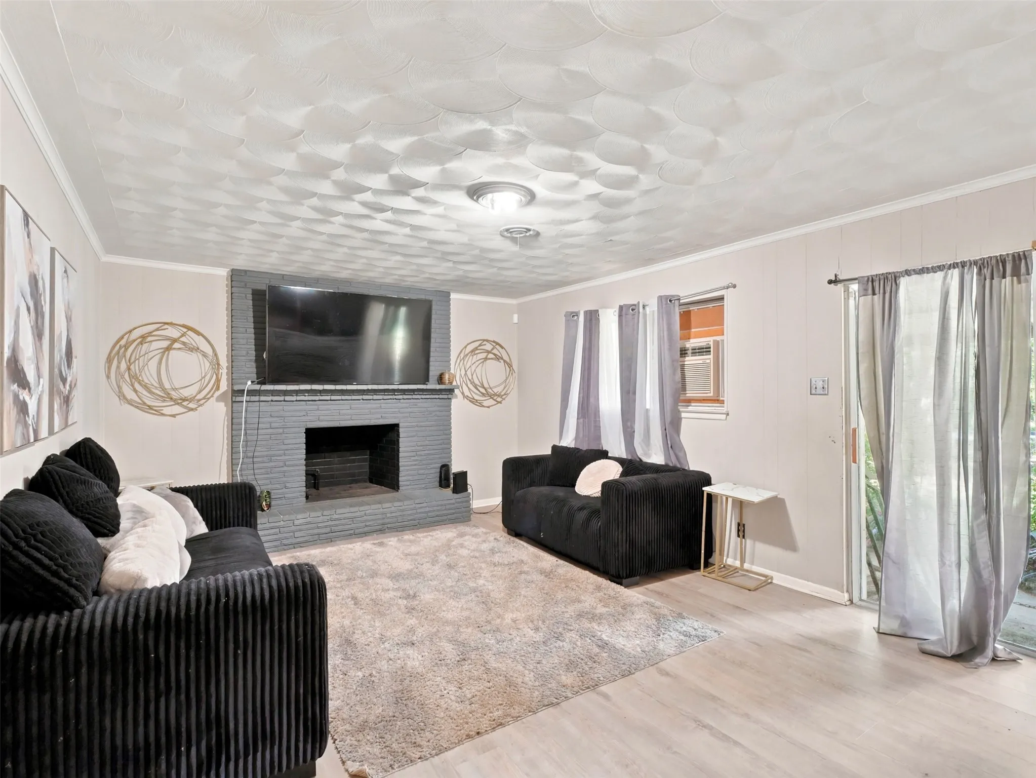 Living area featuring a painted brick fireplace, light wood-finish flooring, and a sliding glass door