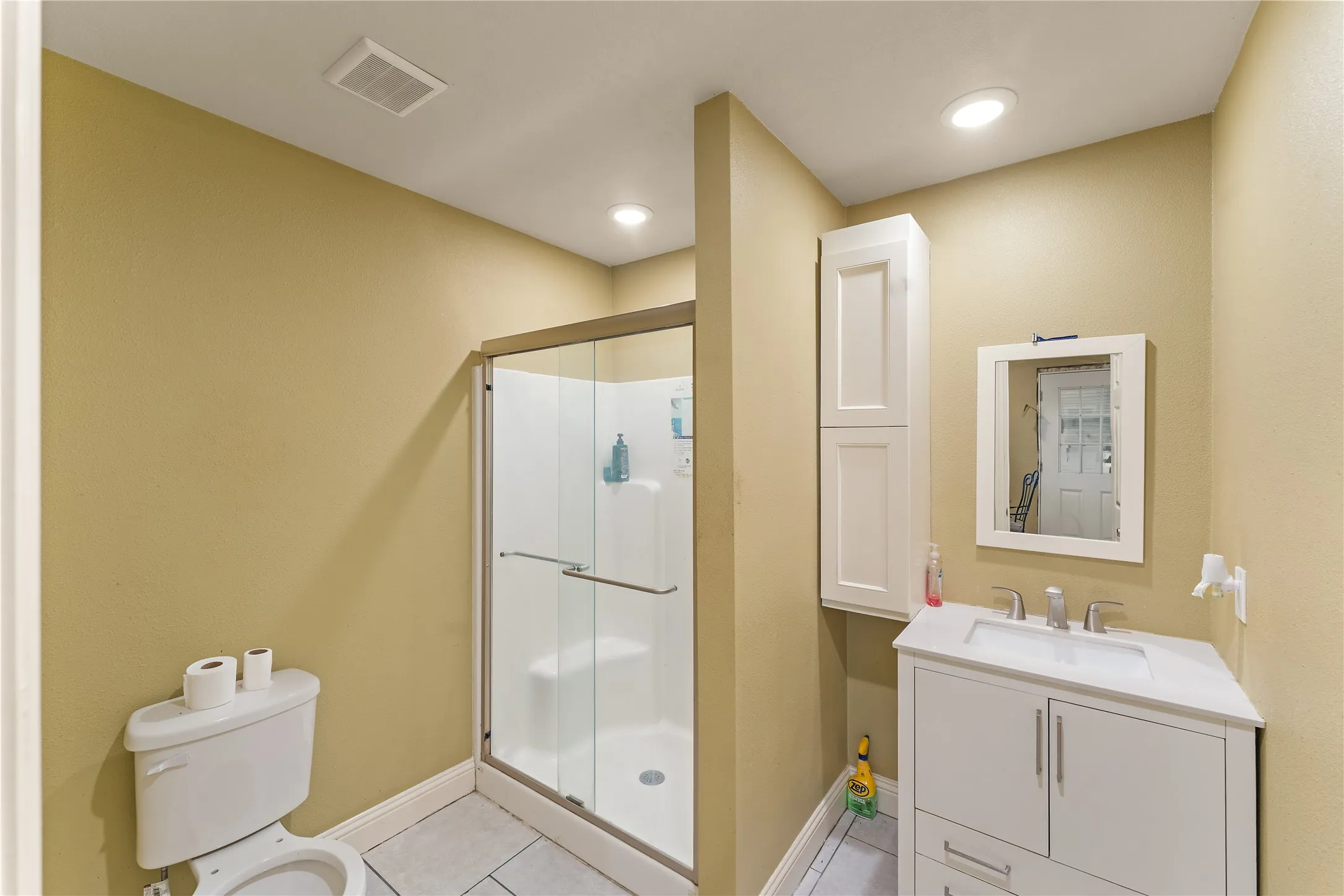Bathroom with a walk-in shower featuring a glass enclosure, a white vanity with an integrated sink, a mirrored medicine cabinet, a wall-mounted storage cabinet, and recessed ceiling lighting