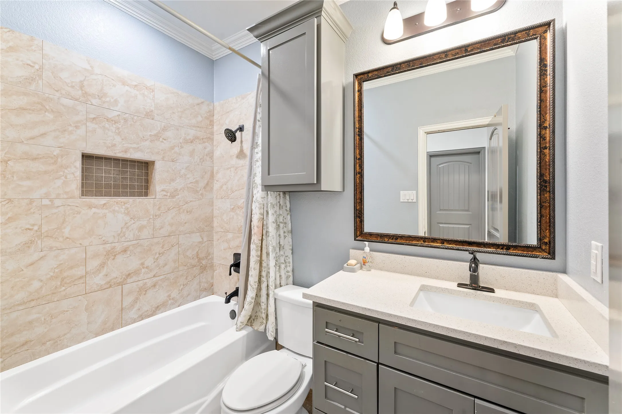 Bathroom featuring a single vanity with light-toned countertop, framed mirror, and gray cabinetry