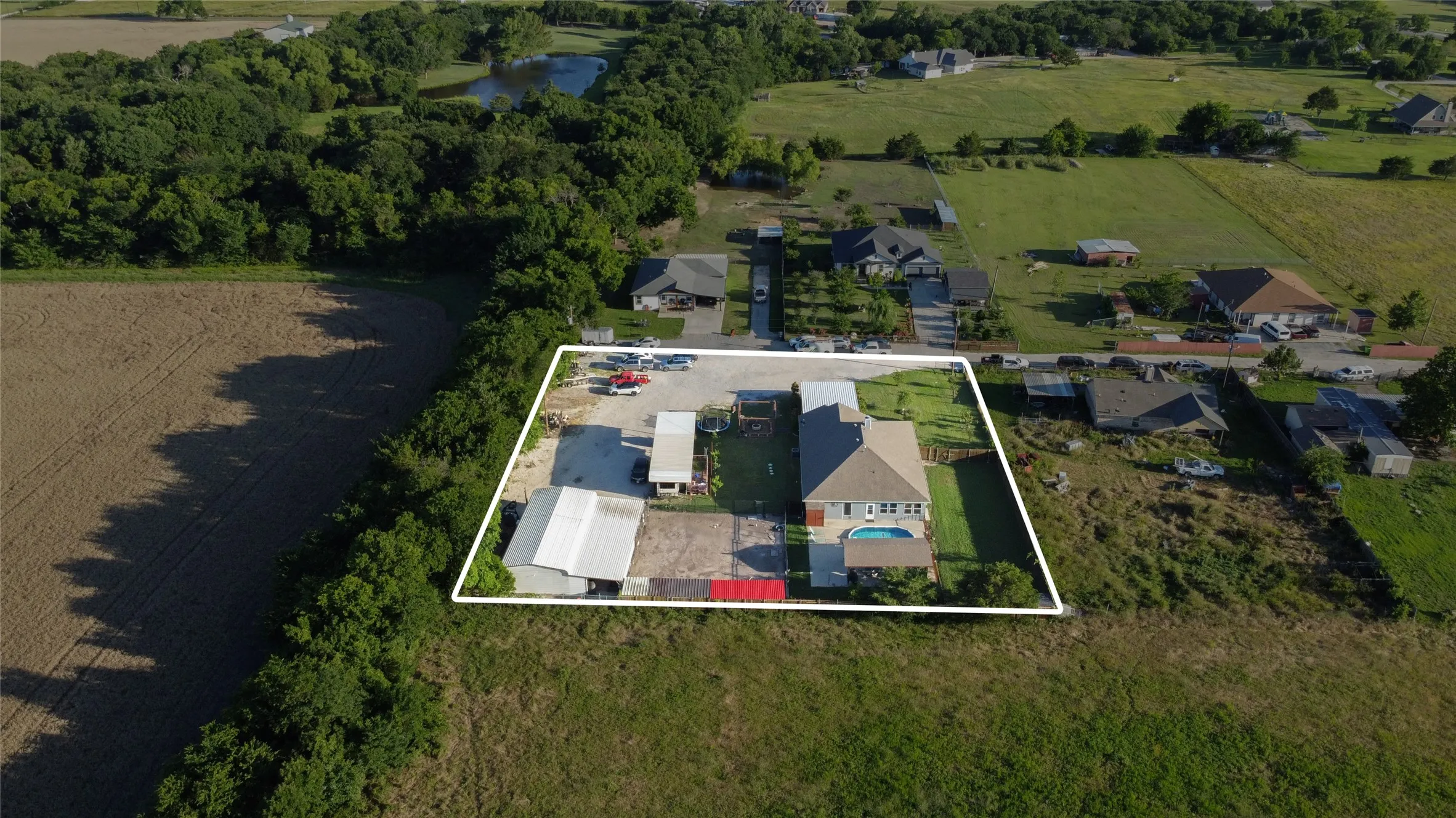Aerial view of a residential property featuring a main house, an inground swimming pool, and an expansive paved area