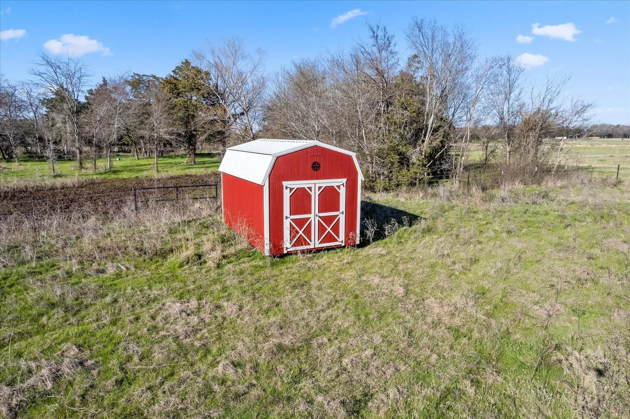 Red storage shed with white trim and a gambrel roof in a grassy field