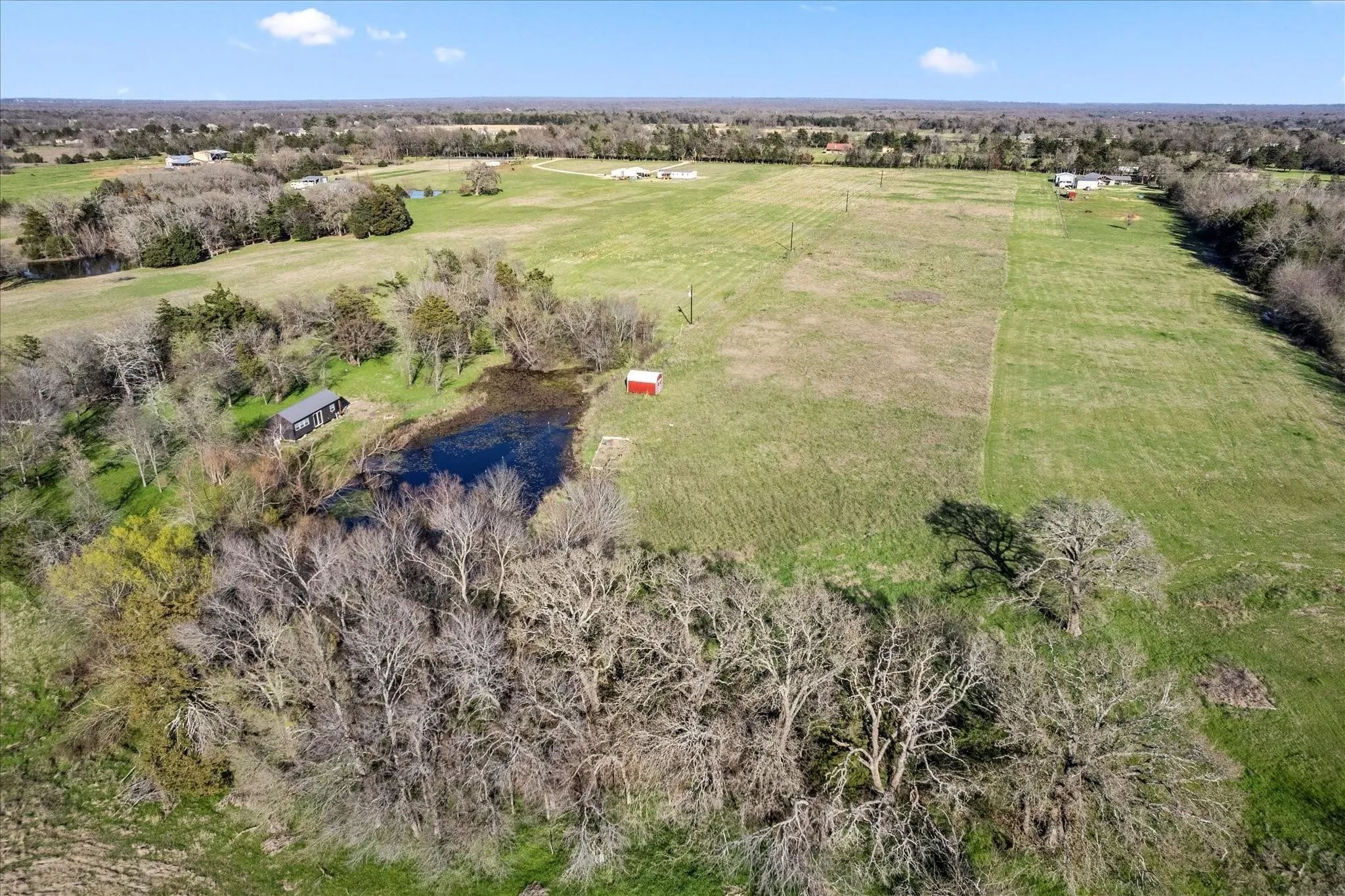Expansive acreage featuring a natural pond, a small red outbuilding, and scattered mature trees