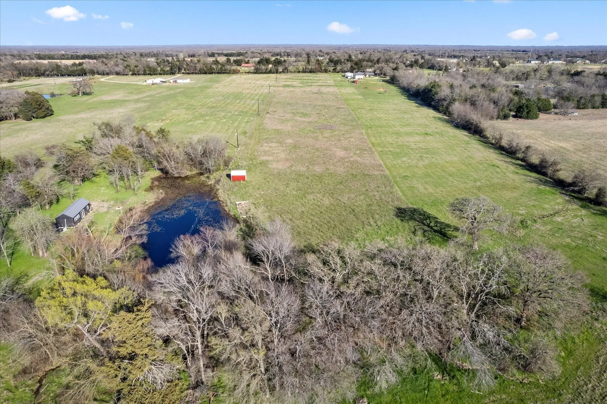 Expansive acreage featuring a natural pond, scattered trees, and a red utility shed