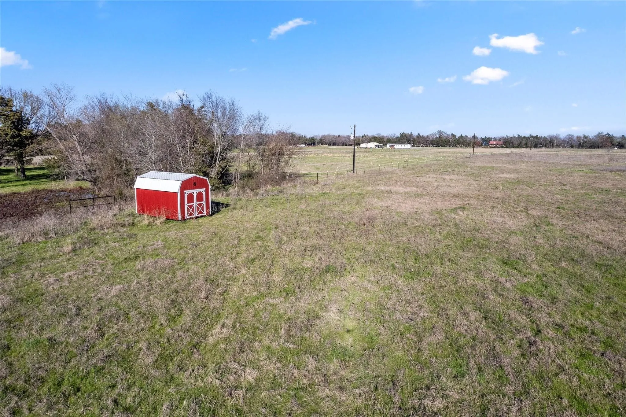 Expansive open field with a red and white storage shed featuring double doors and a metal roof