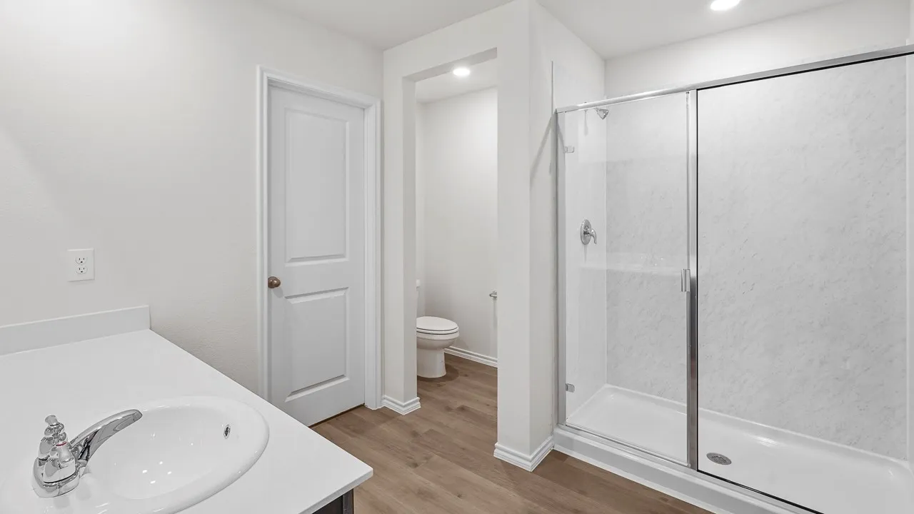 Bathroom featuring a glass-enclosed shower with white paneling, a white vanity with an integrated sink, chrome faucet, and wood-finish flooring