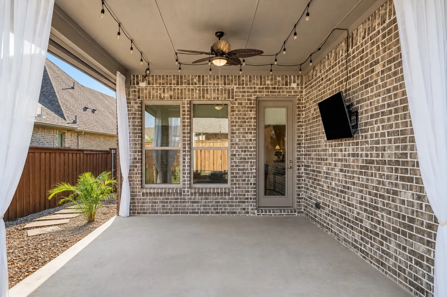 Covered outdoor living area with ceiling fan, TV mount, and generous space for entertaining.